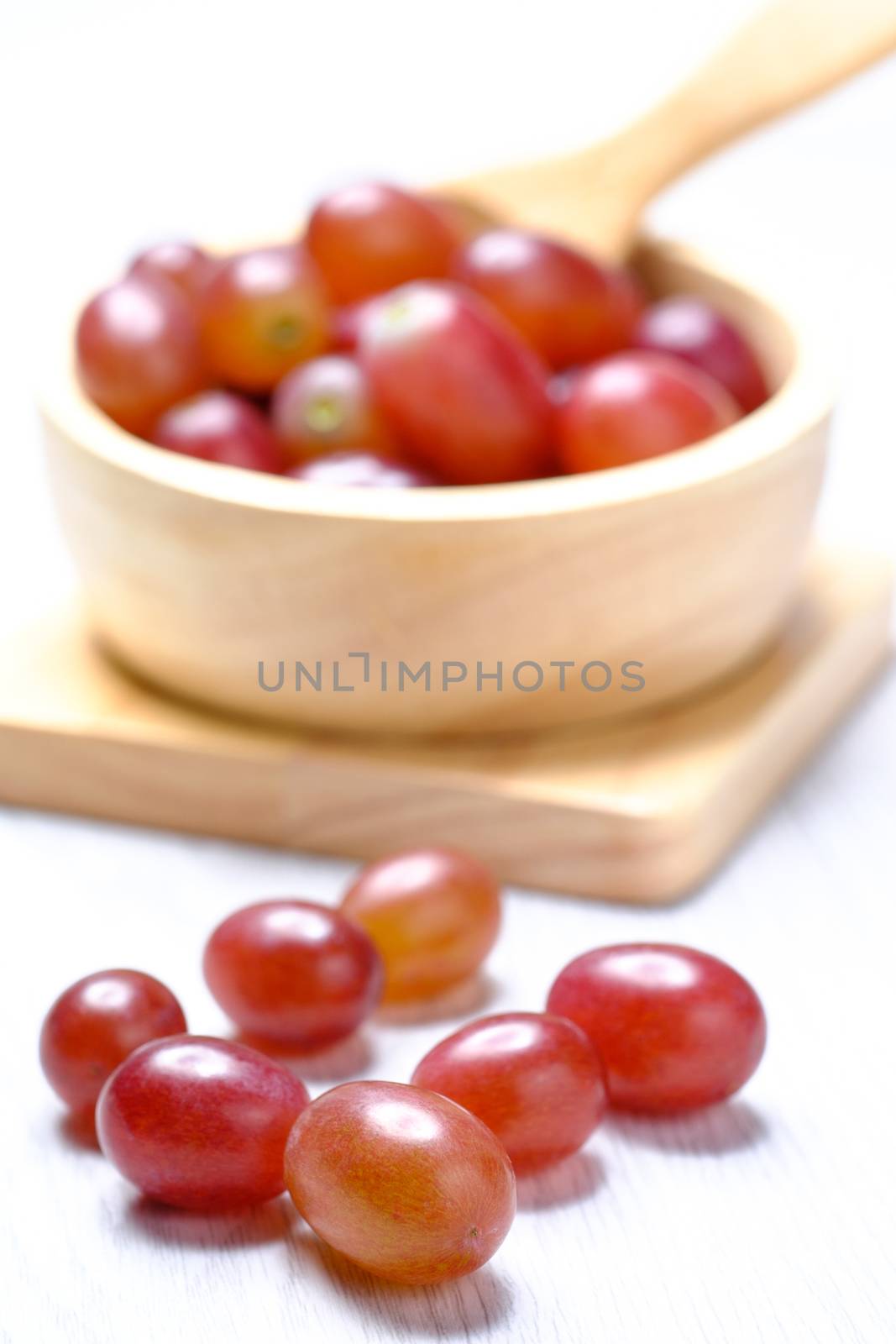 Red grapes in wooden bowl and spoon. they on white wooden table. Clear light by zneb076