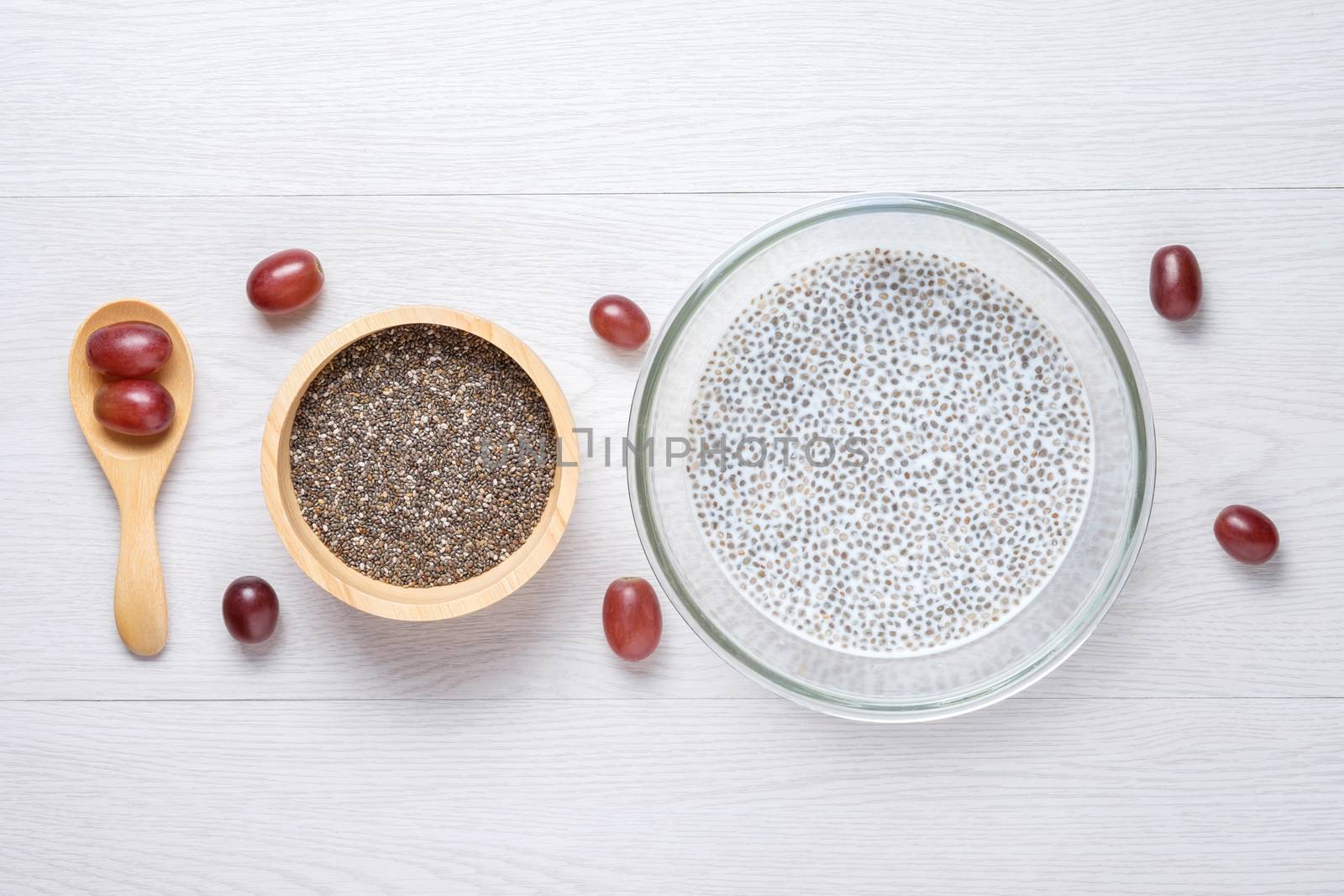 chai seed with milk in grass bowl and raw seed in wooden bowl put next to wooden spoon, use red grape to set beautify this photo