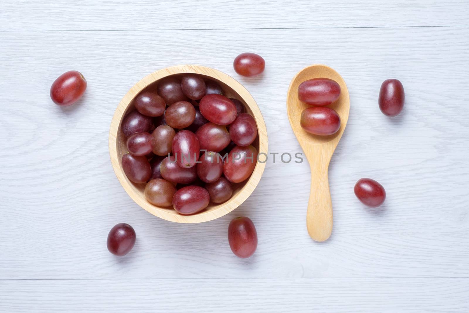 Red grapes in wooden bowl and spoon. they on white wooden table. Clear light
