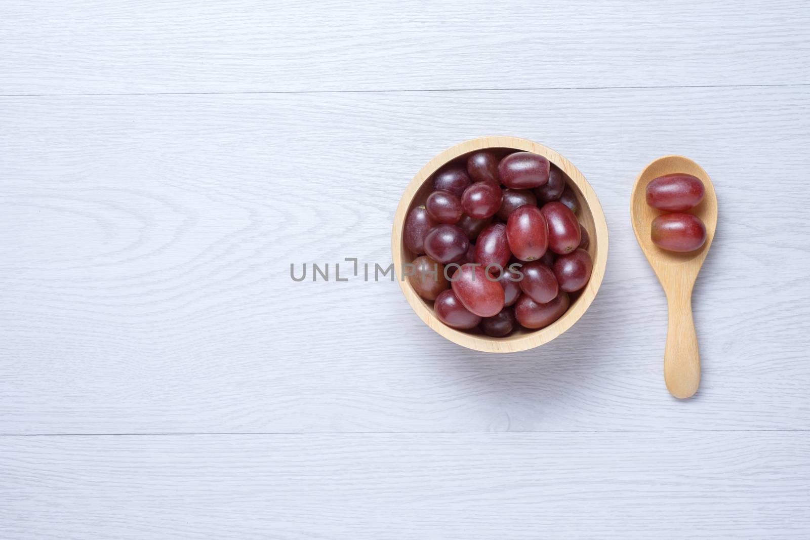 Red grapes in wooden bowl and spoon. they on white wooden table. Clear light.
