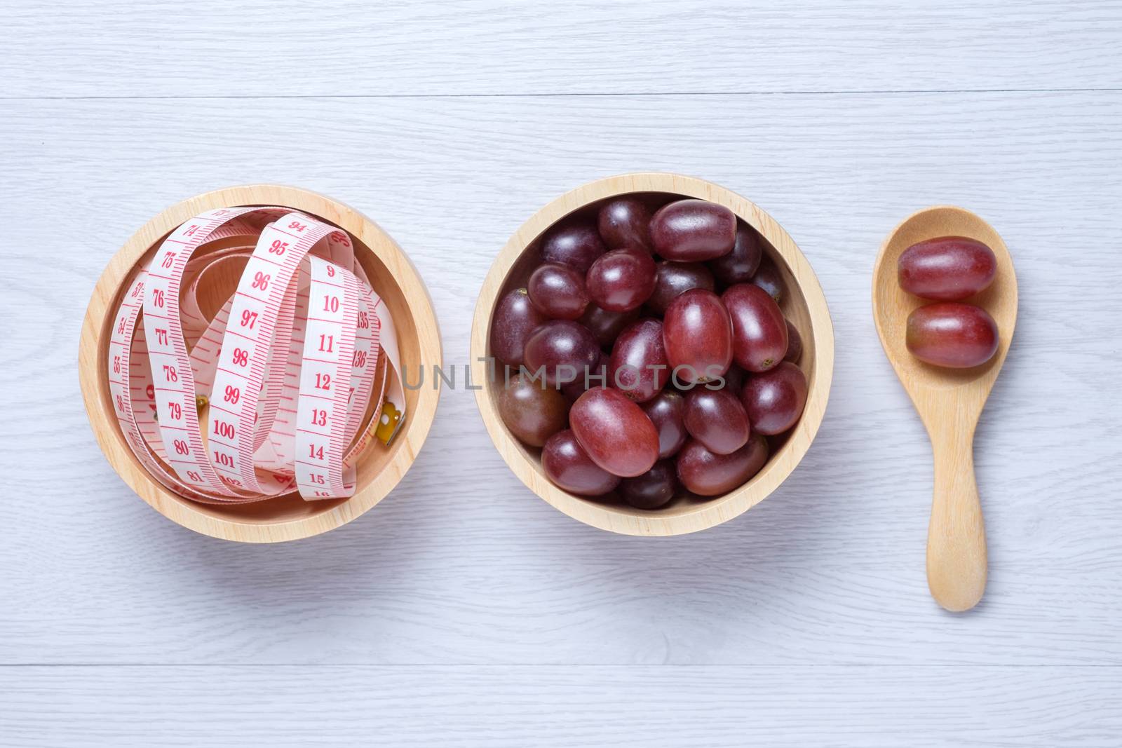 red grapes in wooden bowl and spoon and tape measure in wooden bowl. they on white wooden table. Clear light. this photo use for descript weight loss, diet, eat clean
