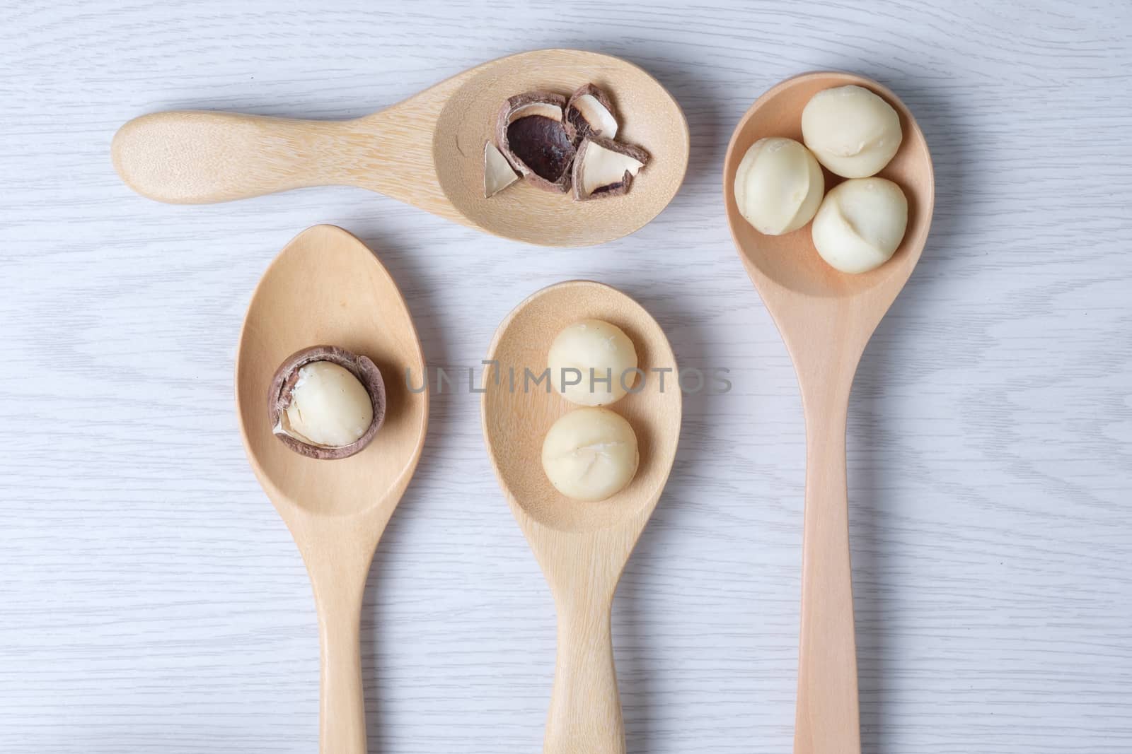 Macadamia nuts and shell in wooden spoons put on white wooden table