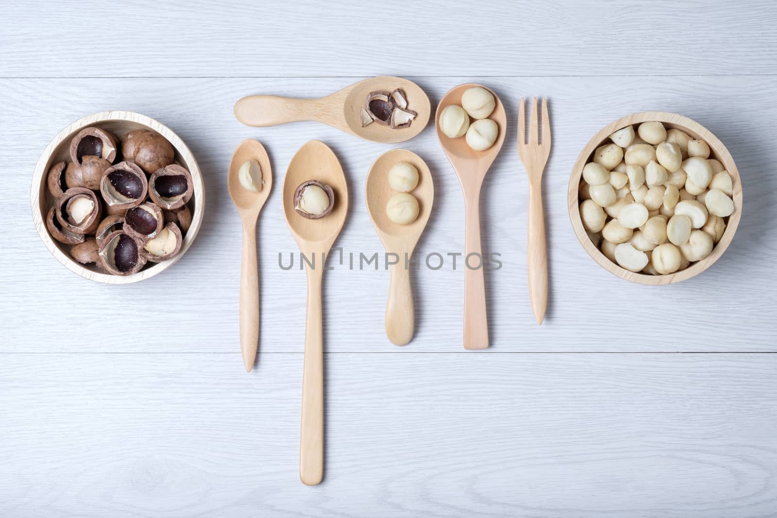 Macadamia nuts and shell in wooden bowl and spoons put on white wooden table
