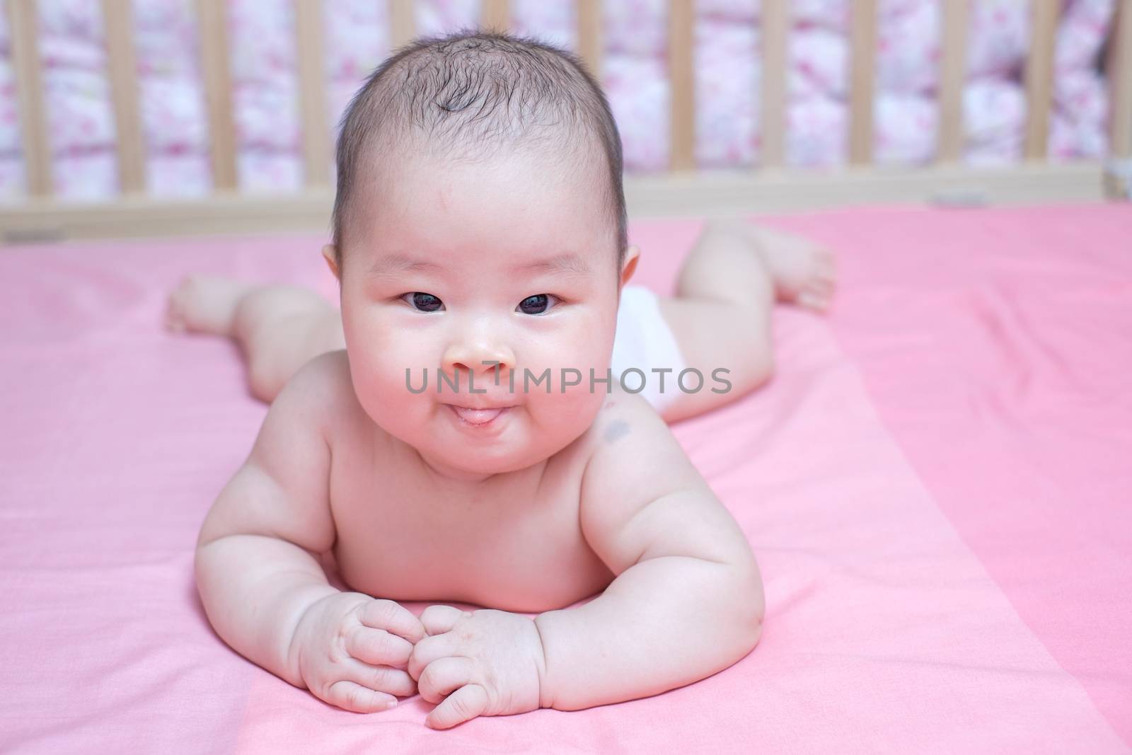 Asian baby girl lie prone on pink bed by zneb076