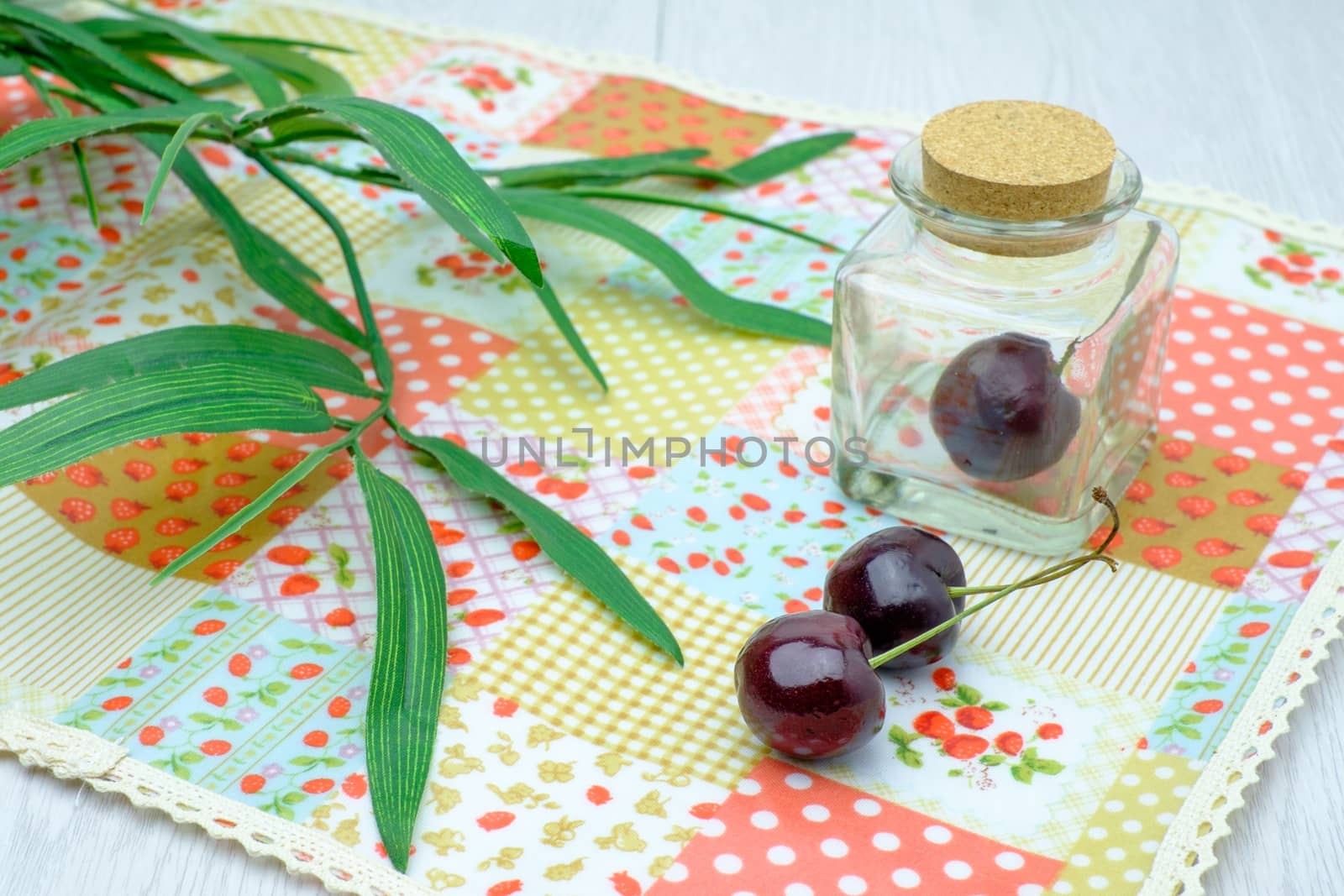cherries on napery and in glass bottle on white wooden table