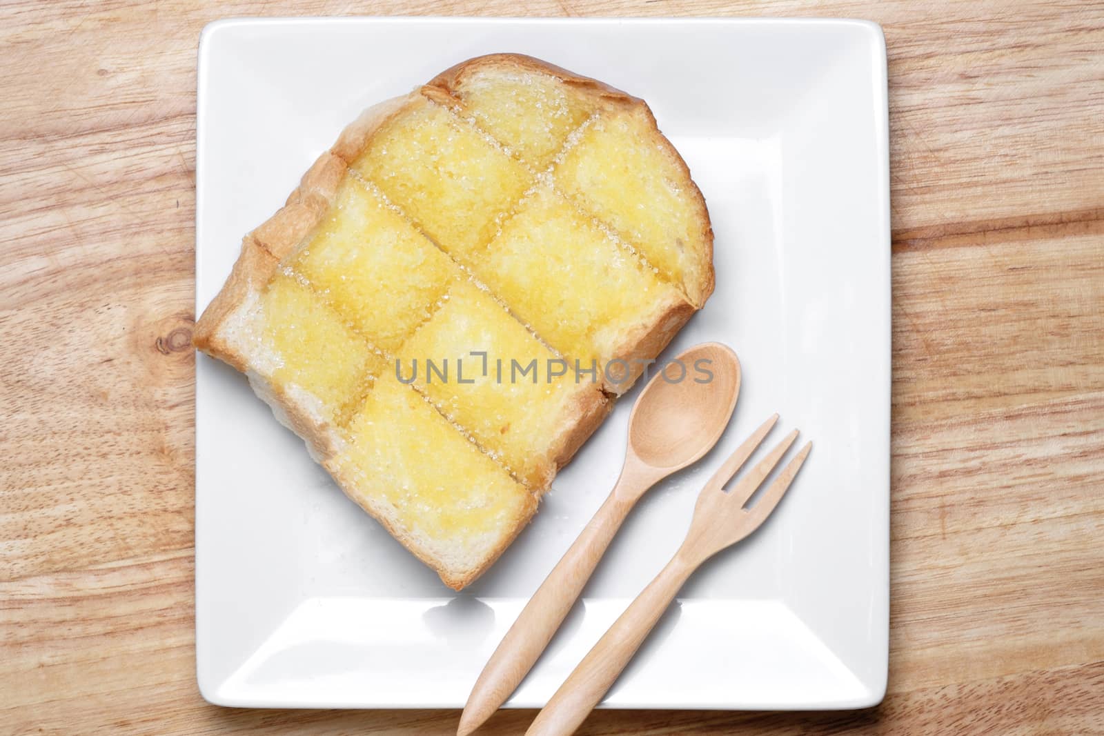 toasted bread on white ceramic dish. toasted bread topping by condensed milk and sugar. wooden spoon and fork ready to eat.