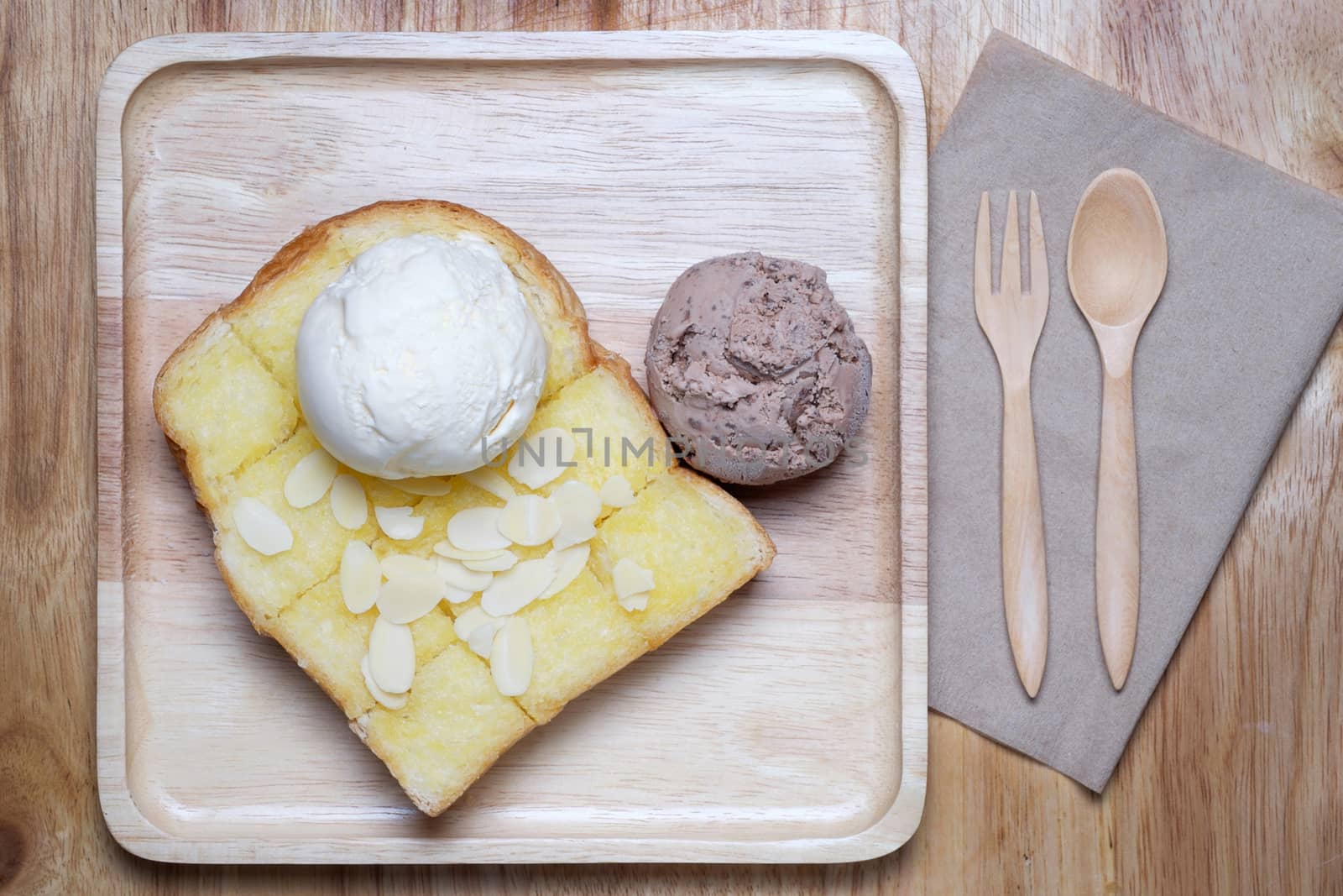 ice creams and almond slice on toast, all put on wooden plate. wooden fork and spoon on table.