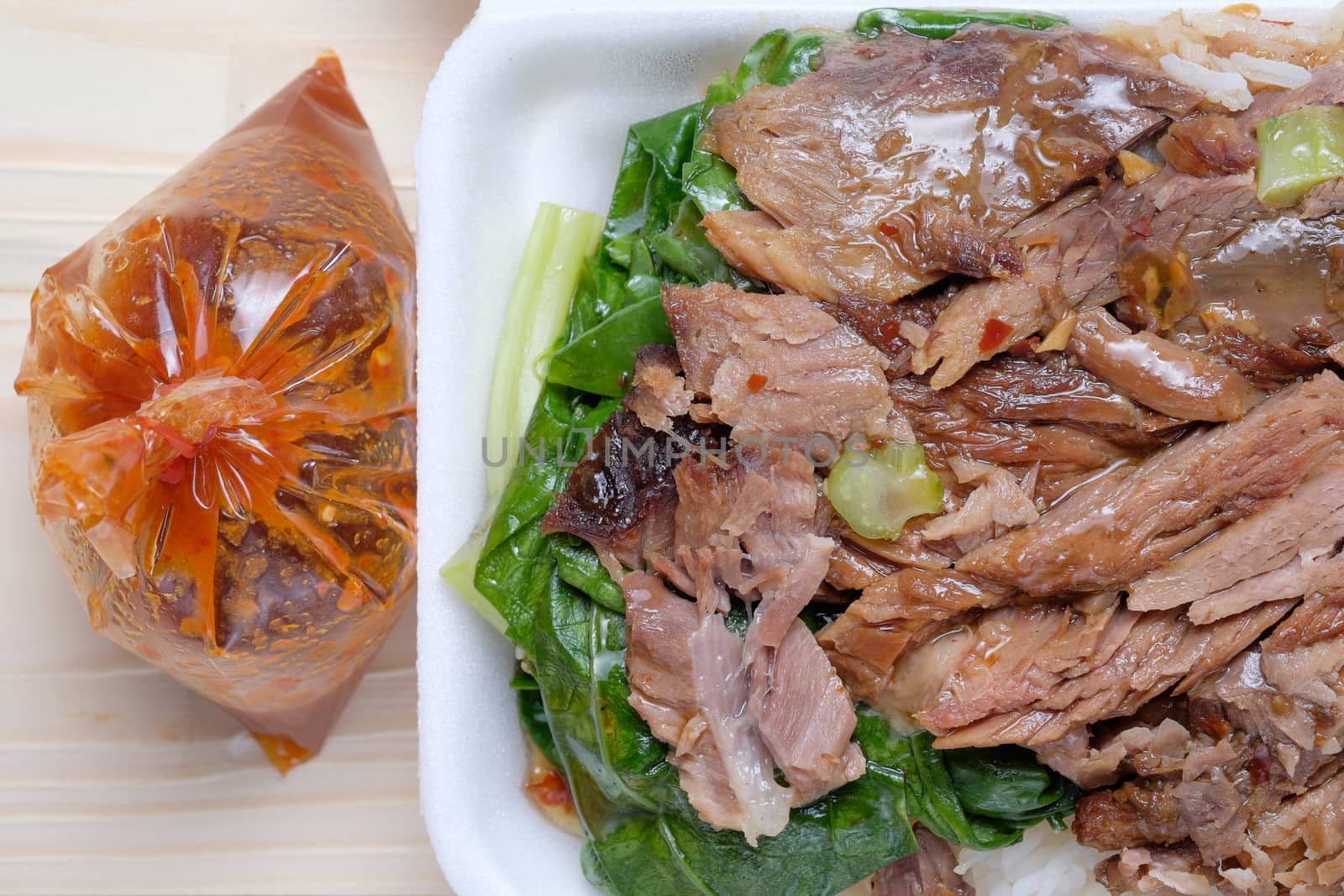 Closeup of Stewed Pork Leg with Rice in foam box and suace in plastic bag on wooden table