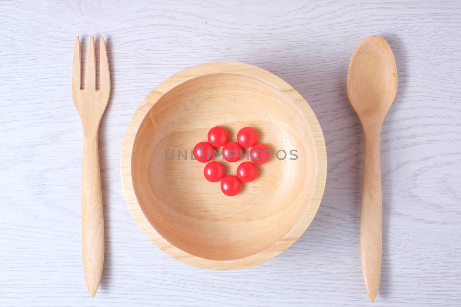 Red pills medicine or vitamin made to heart symbol in wooden bowl