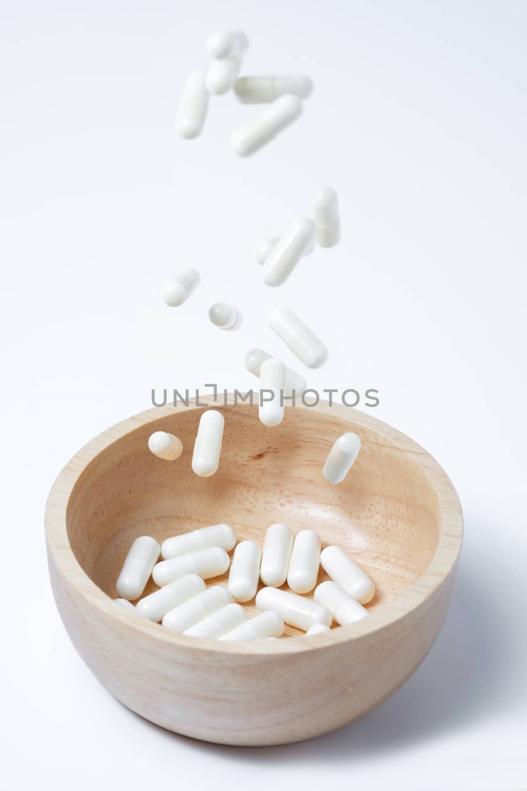 falling of white capsules medicine or vitamin in to wooden bowl