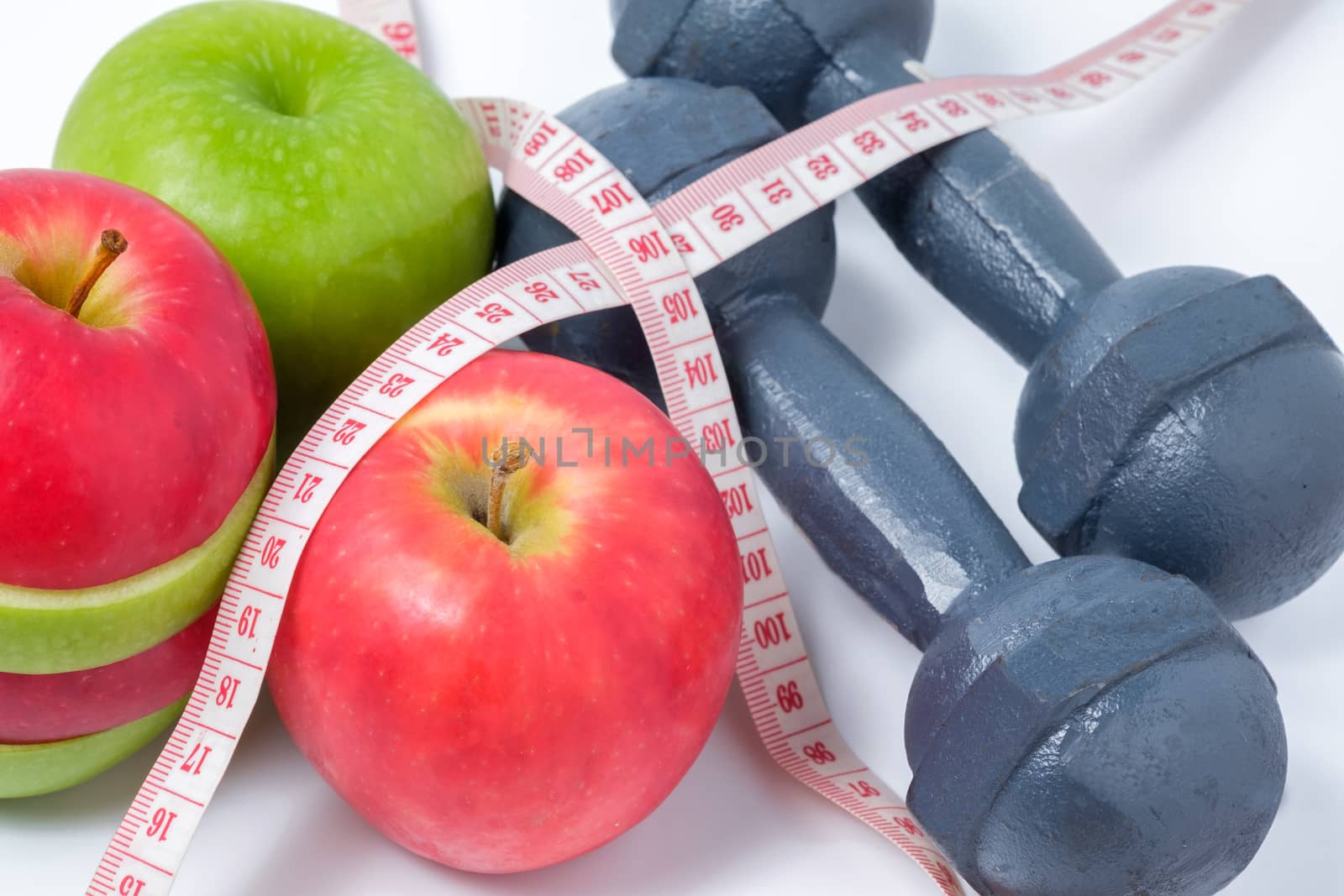 slice red and green apples with dumbbell and waist measure on white background
