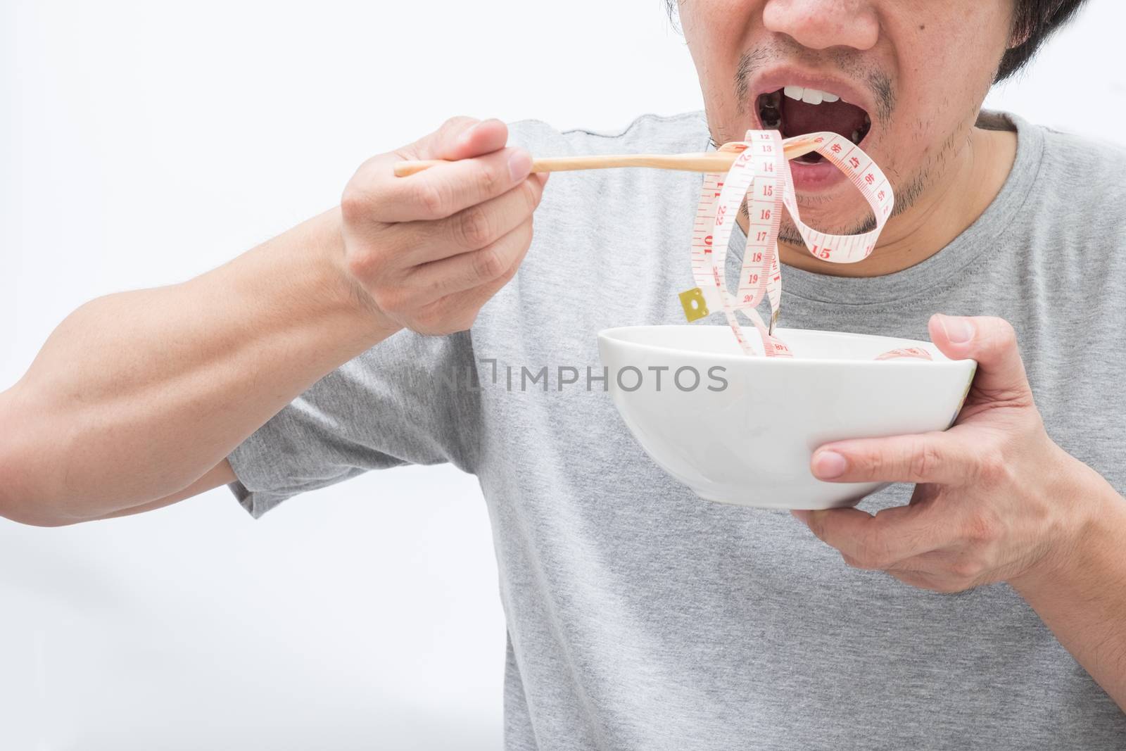Asian man eating waist measure, using wooden fork to put waist measure to his mouth