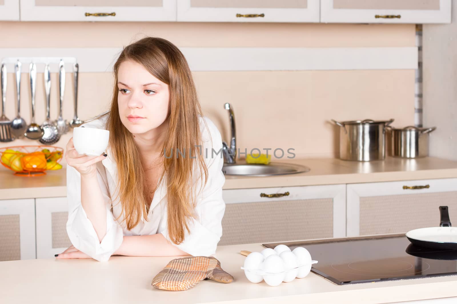 girl in a white men's shirt with long flowing hair is drinking tea in the kitchen in the morning. Horizontal framing