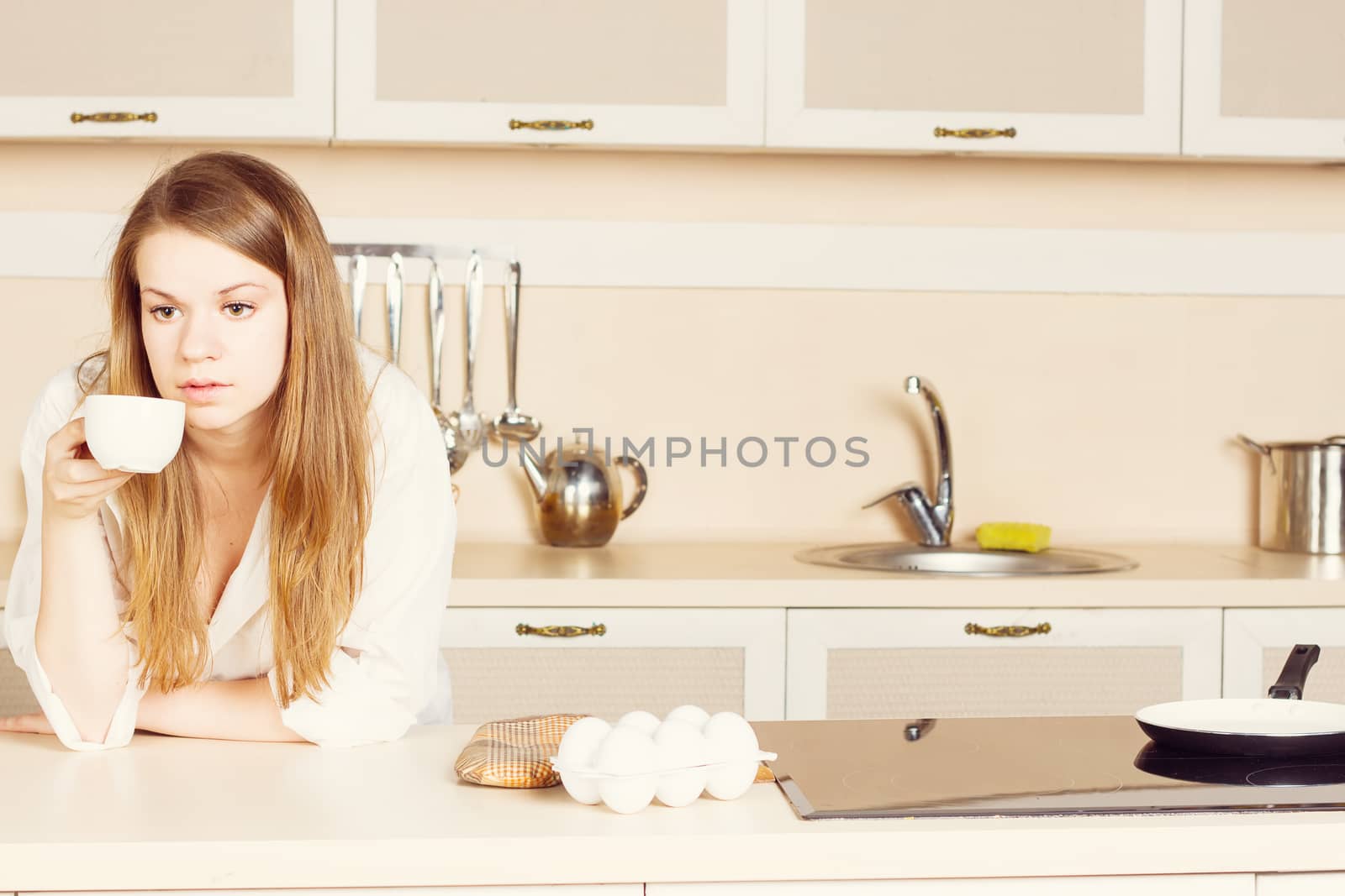 girl in a white men's shirt with long flowing hair is drinking tea in the kitchen in the morning. toning