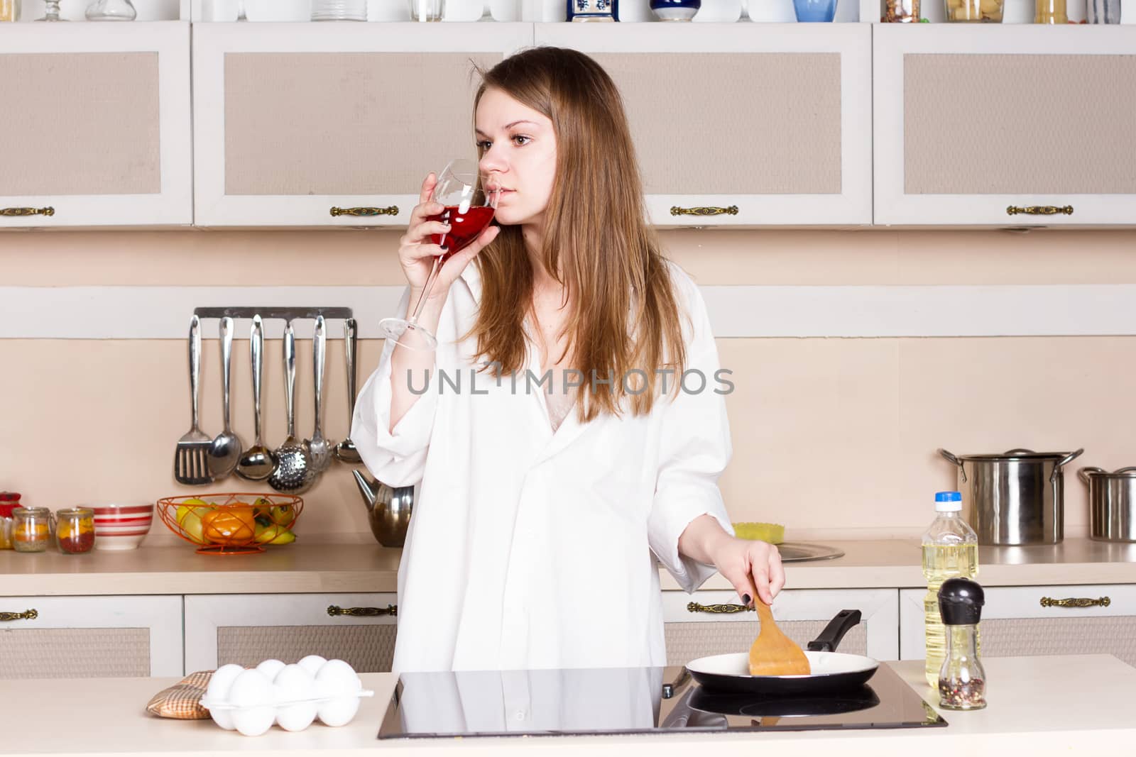 girl in a white men's shirt drinking red wine near the pans