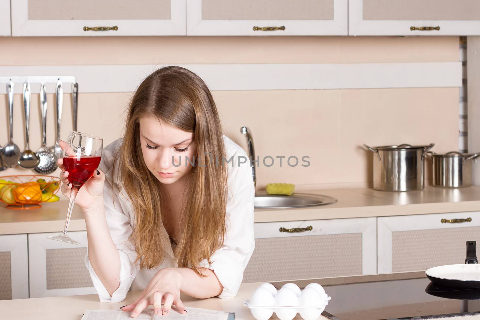 girl in a white men's shirt drinking red wine and reading a book in the kitchen