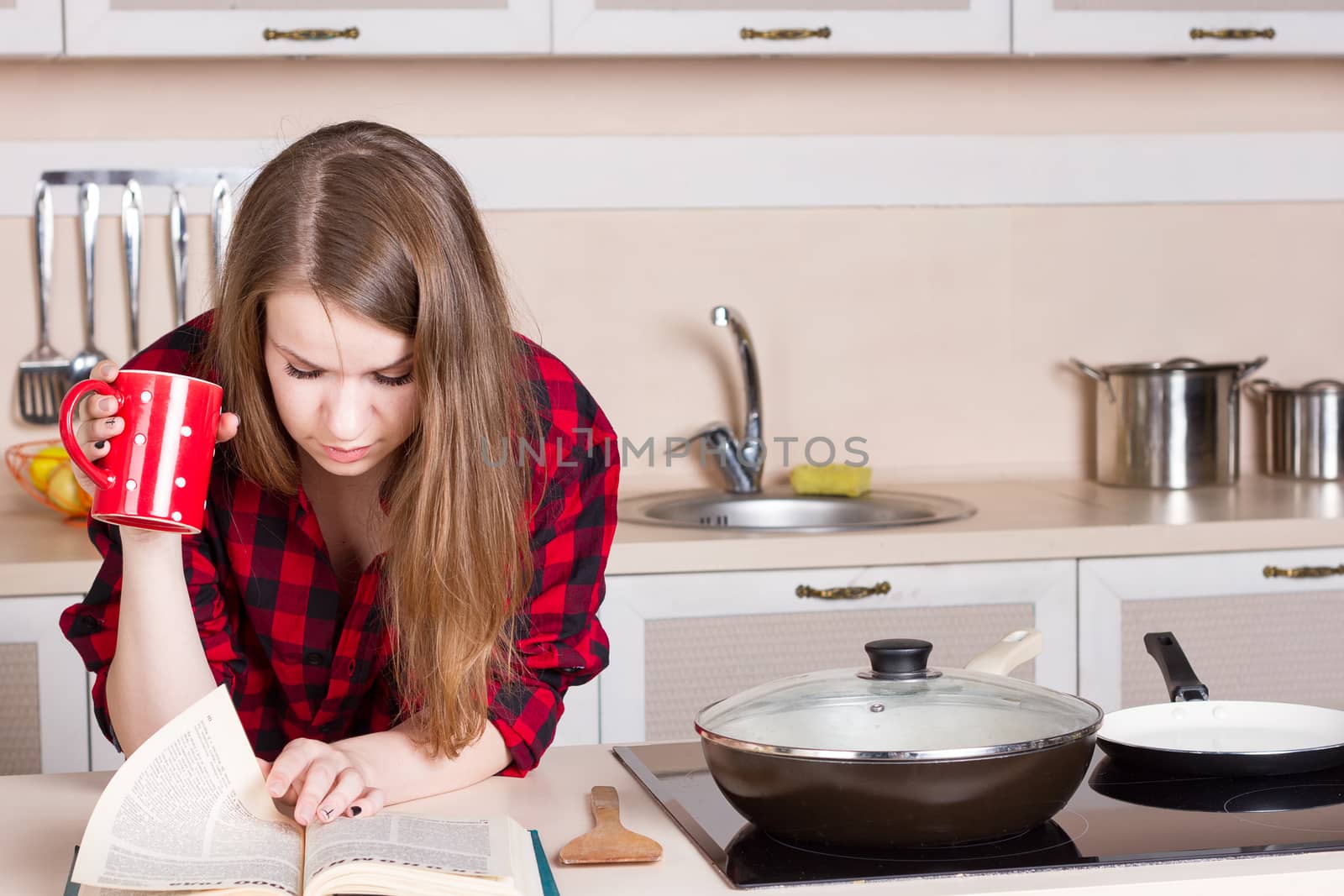 Girl with long flowing hair in a red men's shirt in the kitchen with red cup in his hands