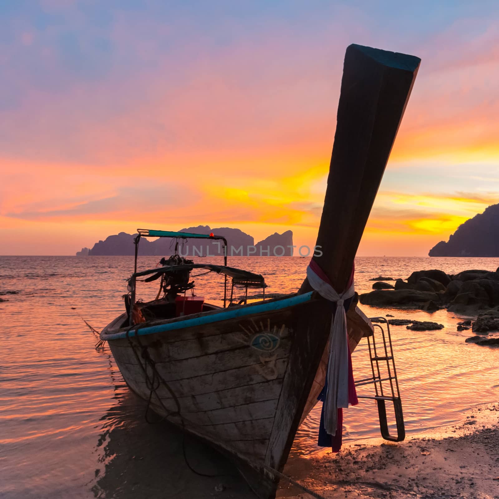 Traditional thai wooden longtail boat on beach of Phi-Phi Don island in sunset. Silhouette of famous Phi Phi Lee island in background. Thailand, Krabi province.