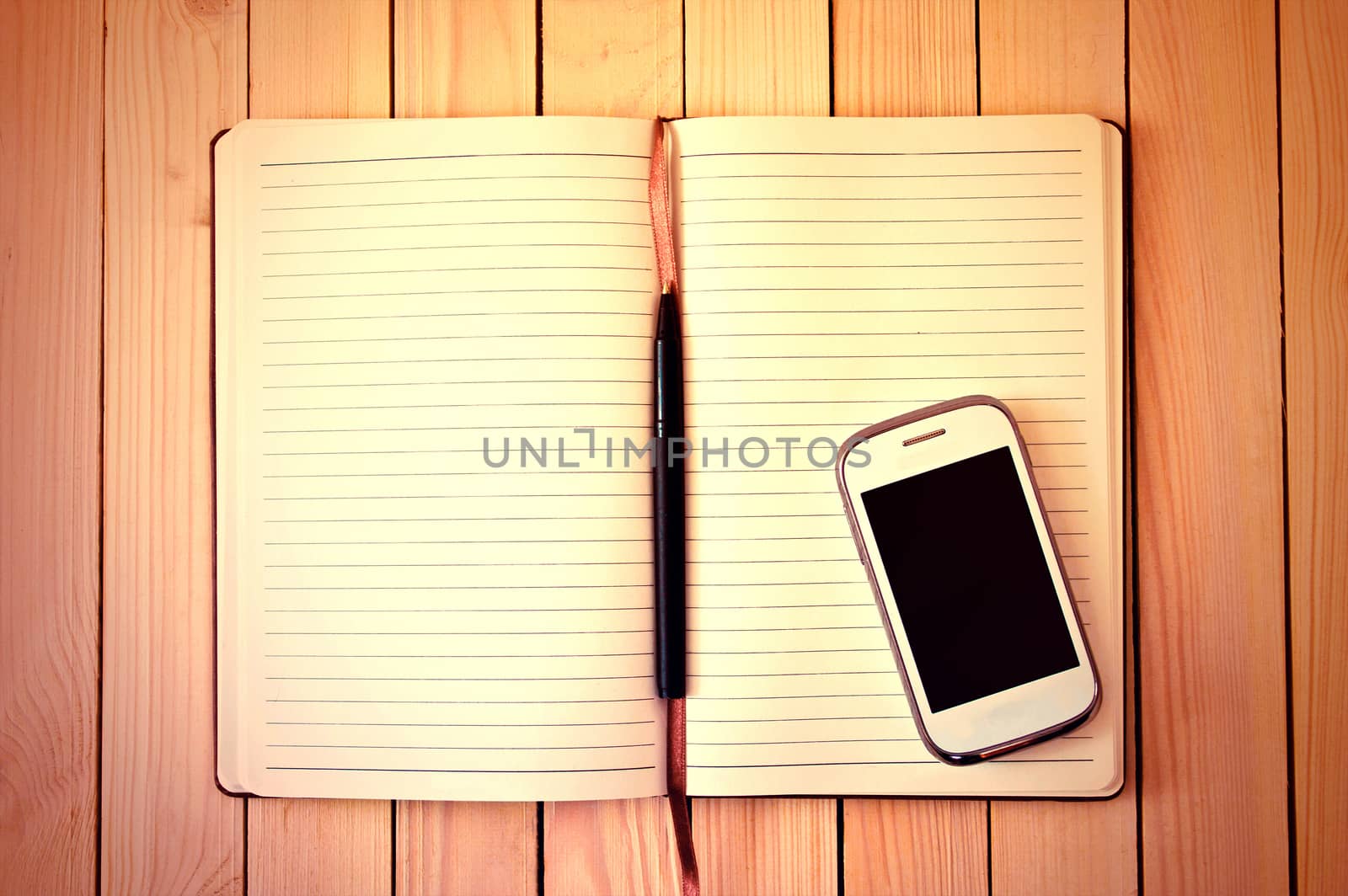 White cell phone, pen and notebook on wooden table. Work space.