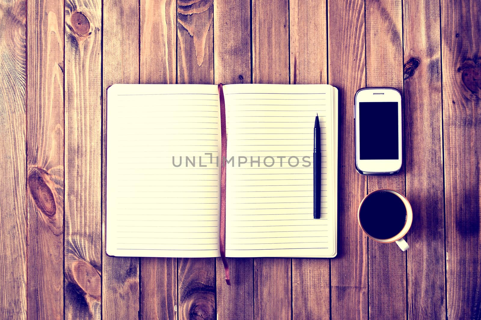 White cell phone, pen, cup of coffee and notebook on wooden table. Work space. Instagram vintage picture.