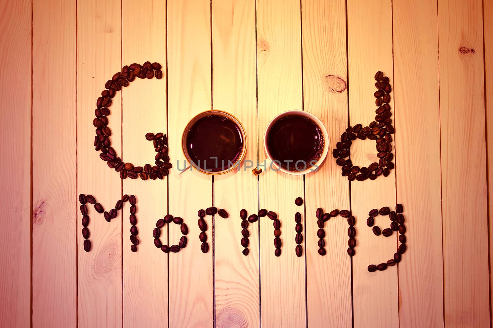 Coffee cups integrated into the Good Morning inscription made with coffee beans on wooden table. Coffee in the morning.