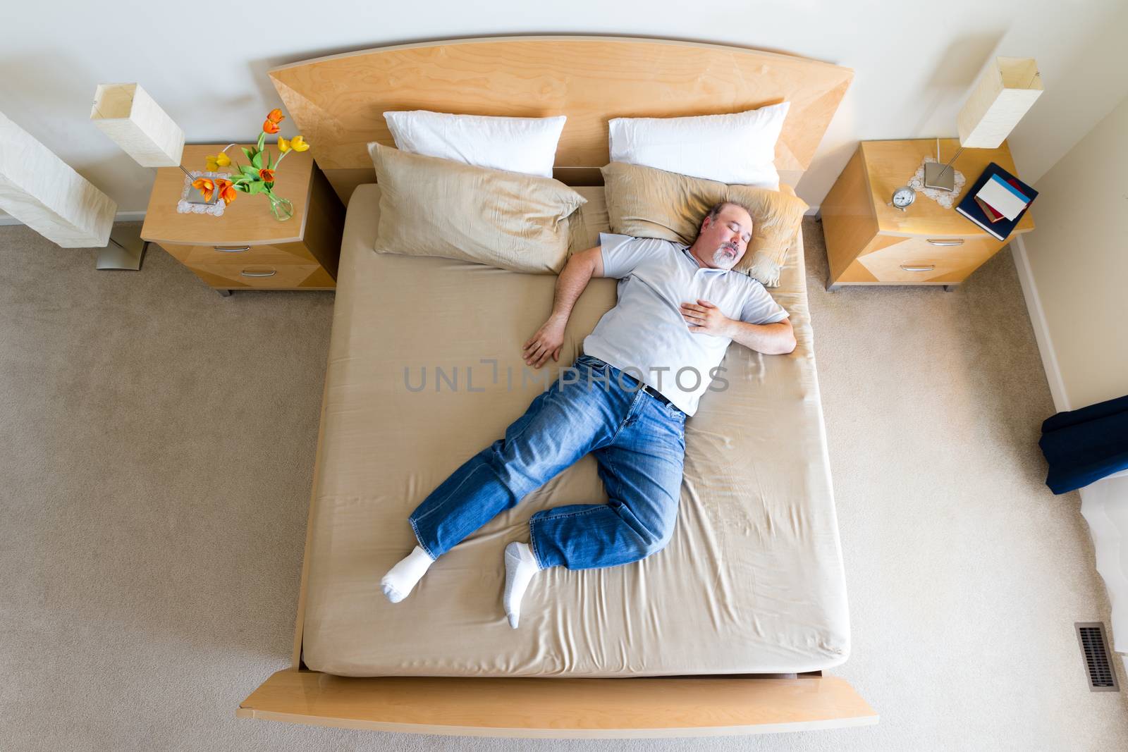 Overhead view of a big overweight middle-aged man with a goatee lying sprawled diagonally in his socks on a king size bed taking a midday nap over the weekend