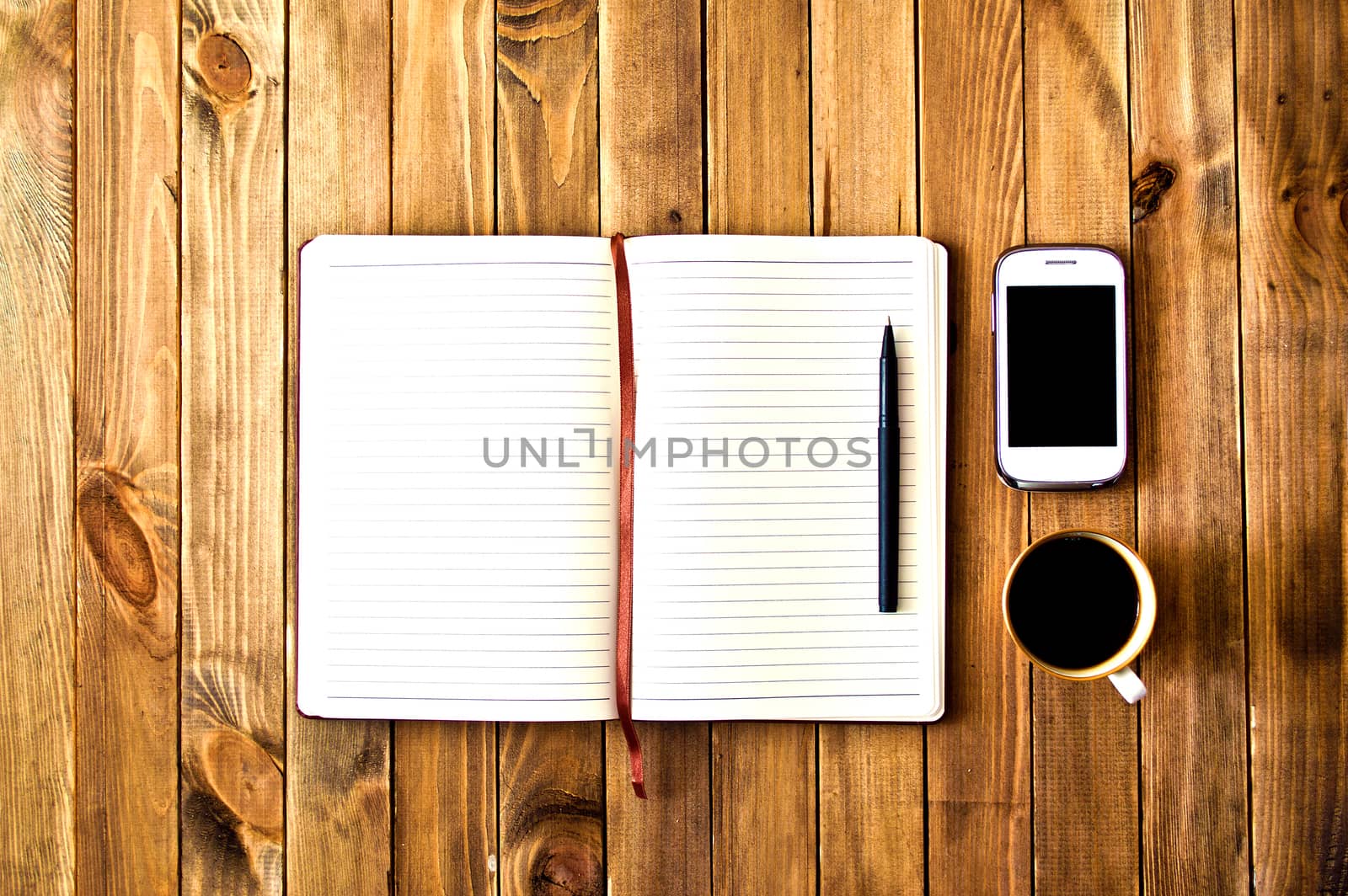 White cell phone, pen, cup of coffee and notebook on wooden table. Work space. Instagram vintage picture.