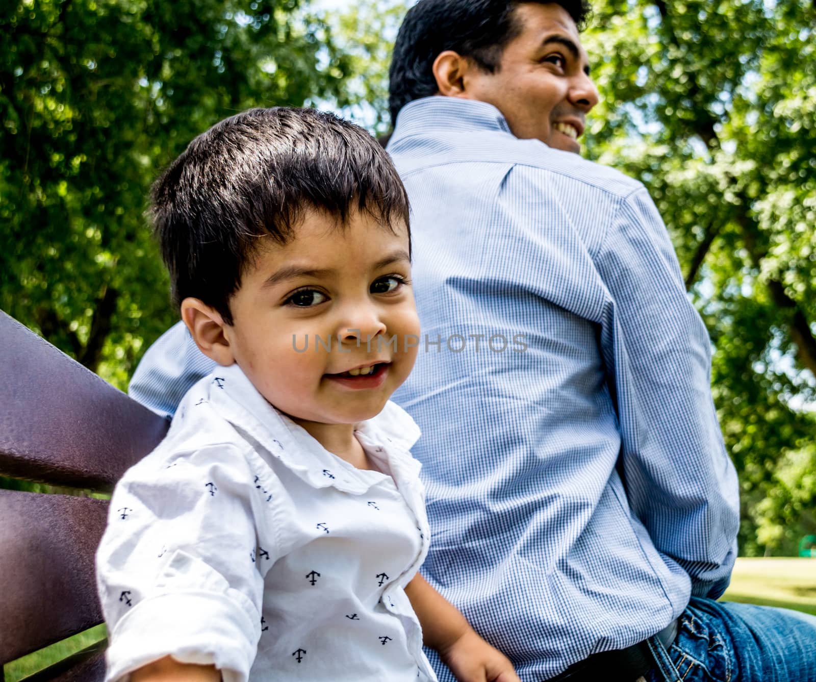 Latino father and son sitting outside on a bench