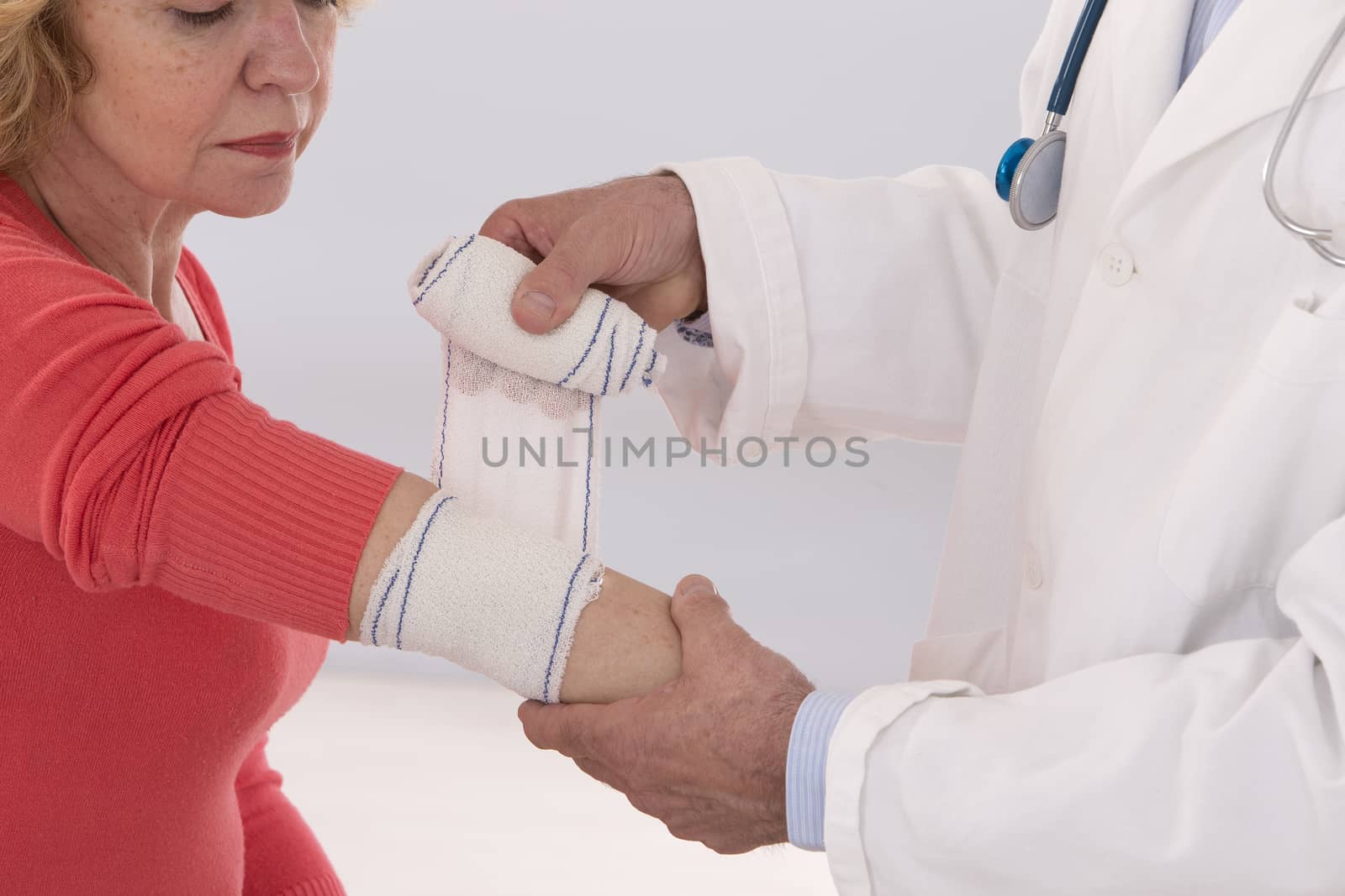 doctor giving first aid to female patient with painful elbow in medical office by JPC-PROD