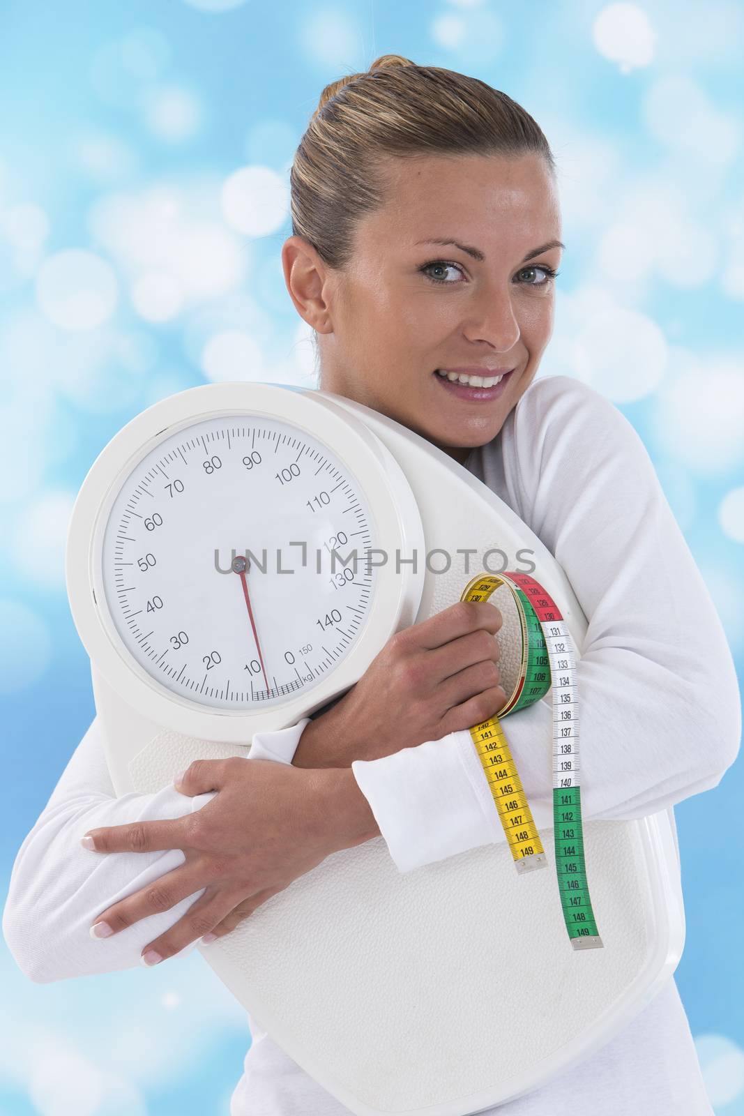 happy young woman holding bathroom scales isolated on blue