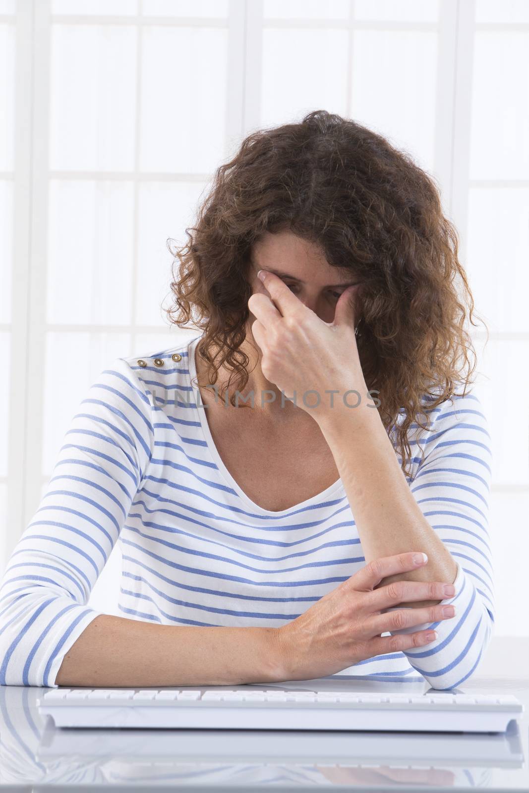 Businesswoman with hands covering her face, in front of desktop