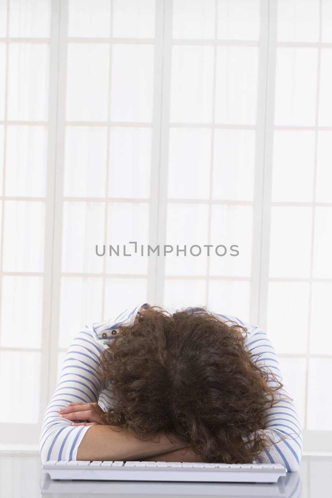 Tired   businesswoman with head on keyboard  in a bright office