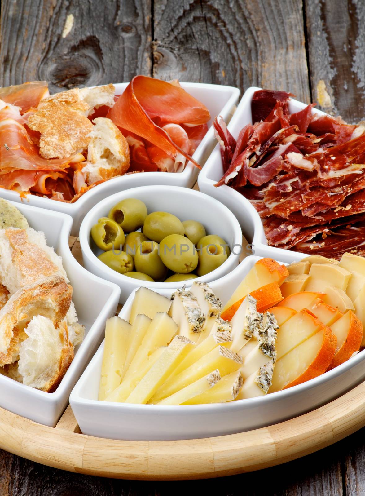 Arrangement of Spanish Snacks with Various Cheeses, Bread Sticks, Jamon, Cured Ham and Green Olives on Serving Plate closeup on Wooden background