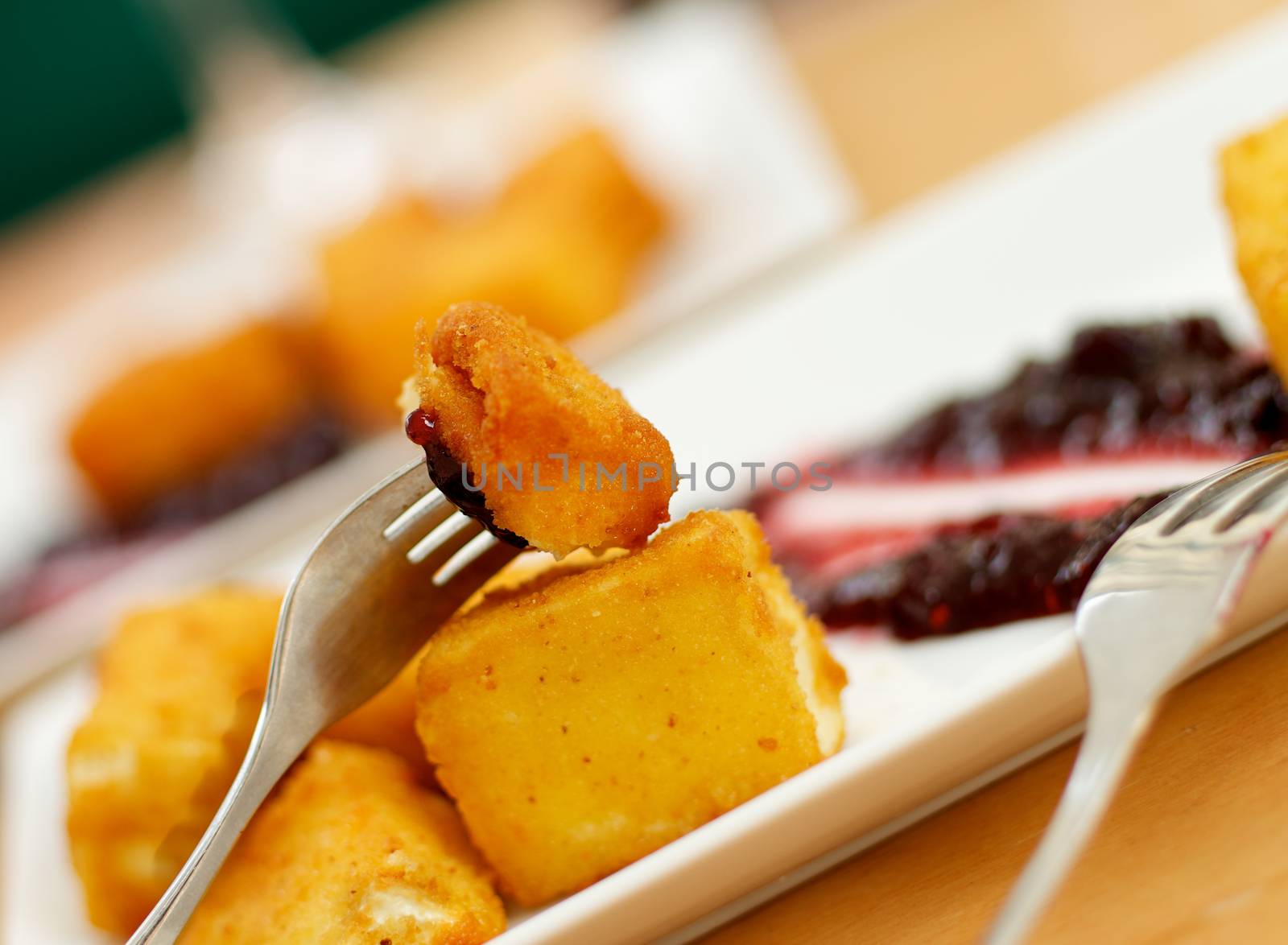 Breaded and Fried Camembert Cheese Served on White Plate with Cranberry Jam and Silver Forks. Focus on Foreground 
