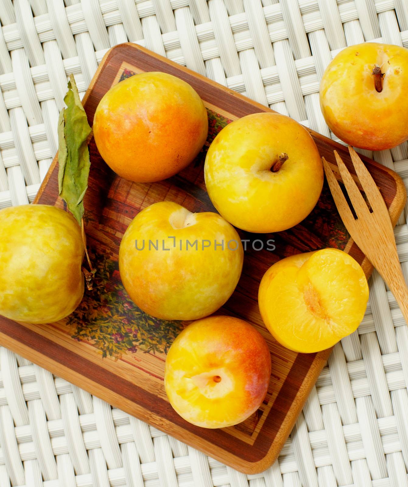 Fresh Ripe Yellow Plums on Wooden Plate with Wooden Fork closeup on Wicker background