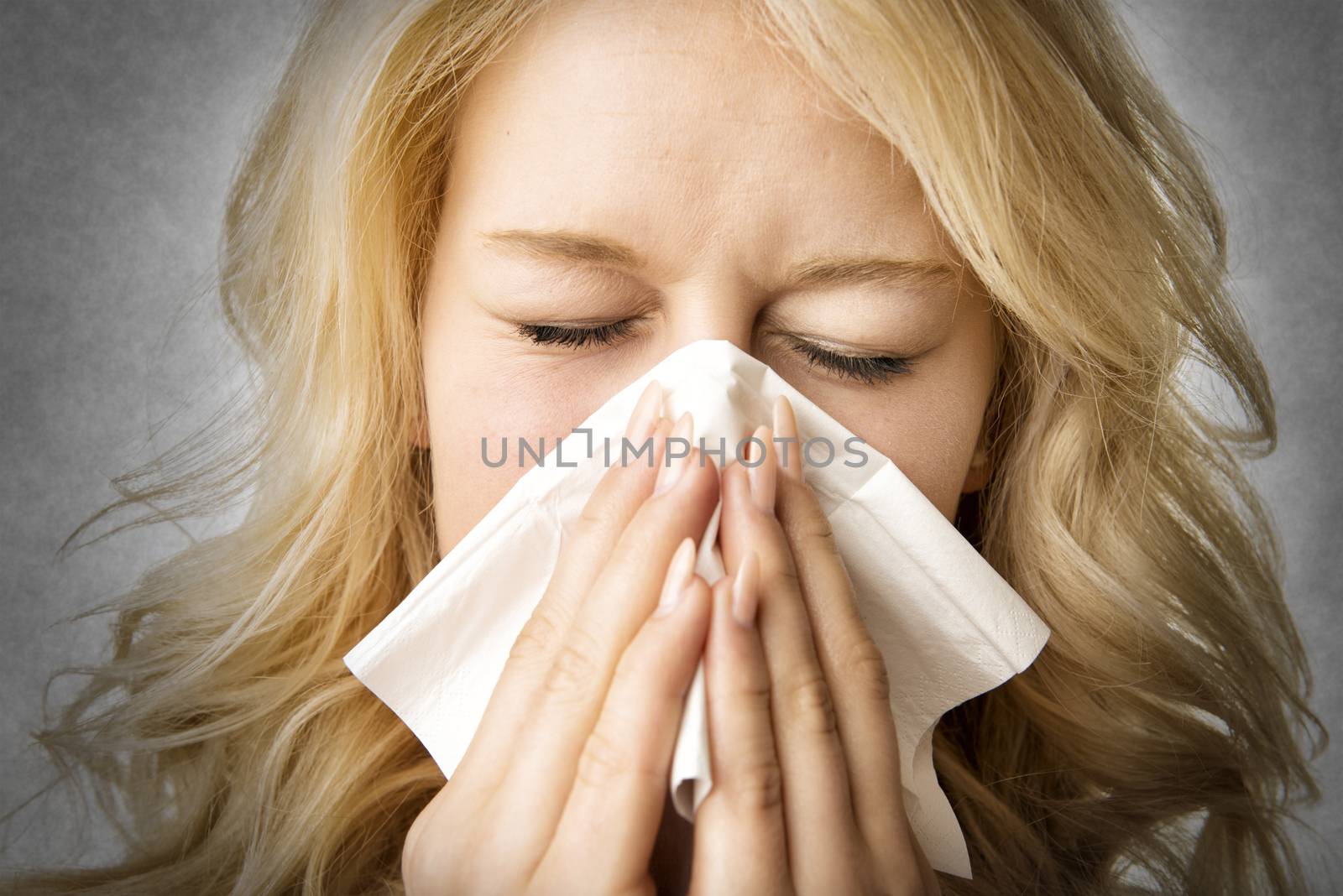 Portrait of a ill blond woman who is sneezing in a tissue