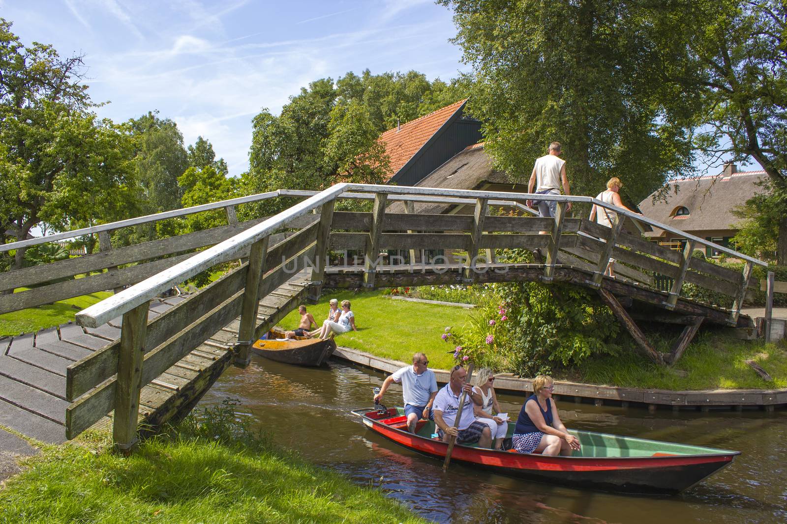 GIETHOORN, NETHERLANDS - AUGUST 05, 2015: Unknown visitors in the sightseeing boating trip in a canal in Giethoorn. The beautiful houses and gardening city is know as "Venice of the North".
