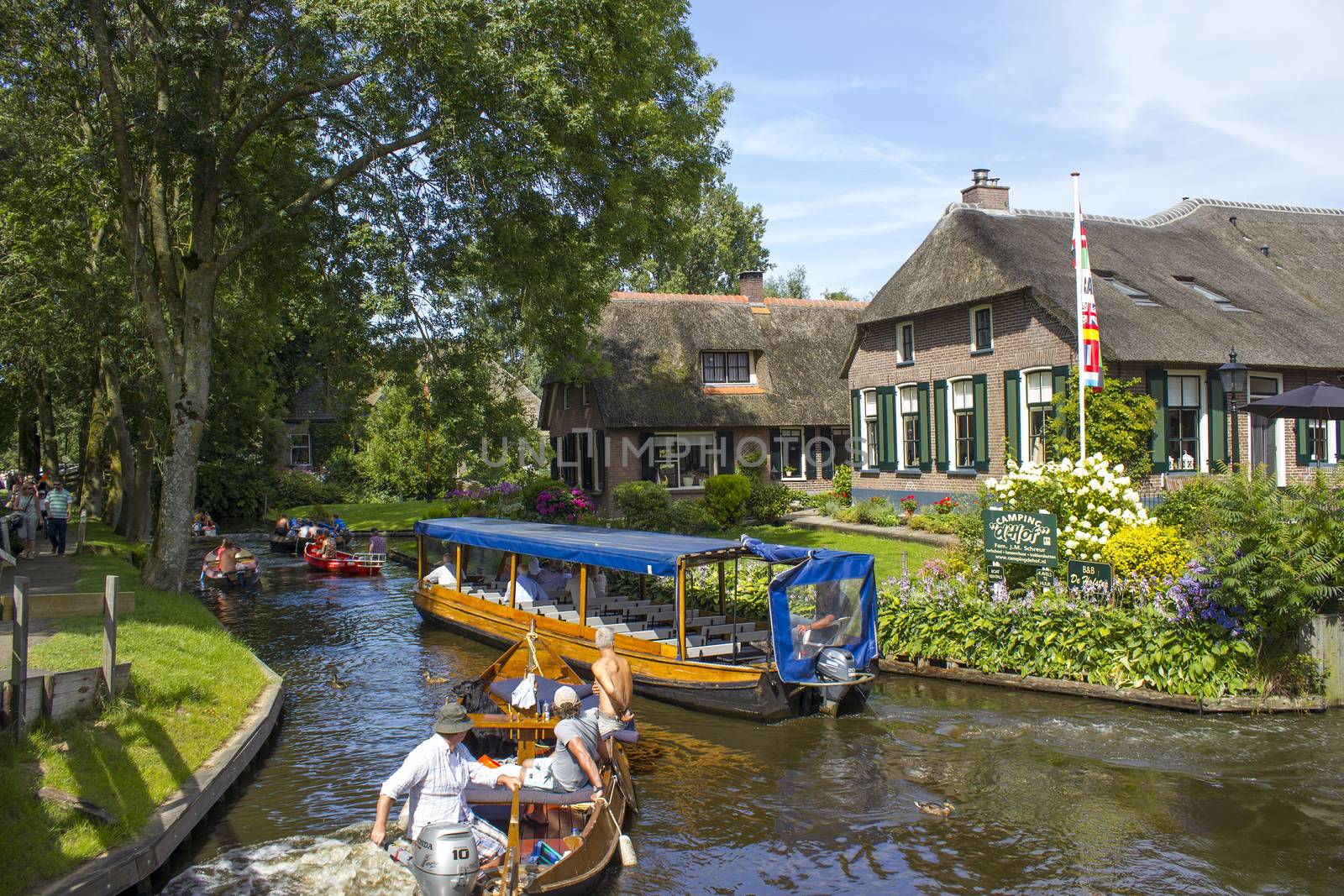 GIETHOORN, NETHERLANDS - AUGUST 05, 2015: Unknown visitors in the sightseeing boating trip in a canal in Giethoorn. The beautiful houses and gardening city is know as "Venice of the North". 