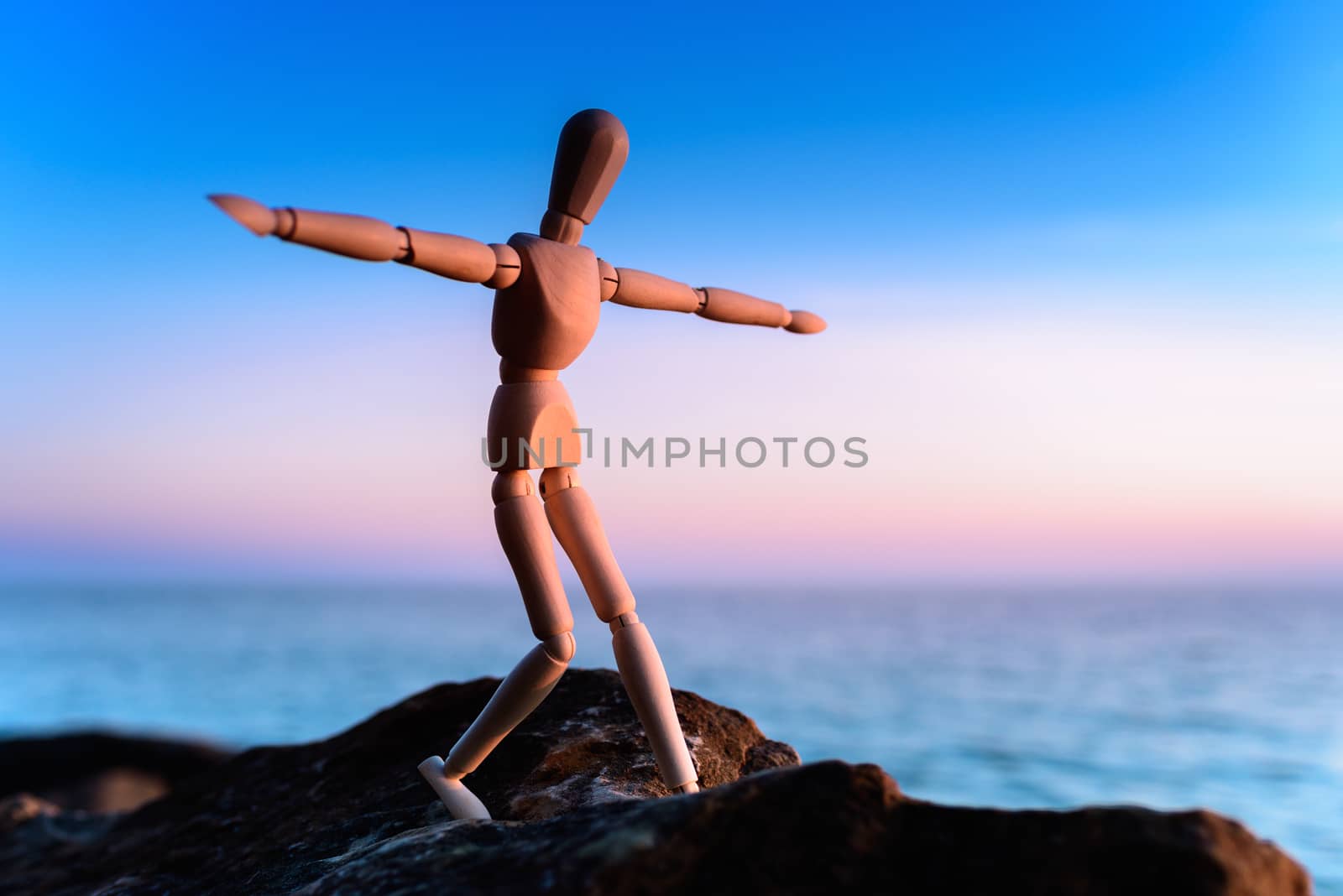 Wooden man stands on the top of sea boulder