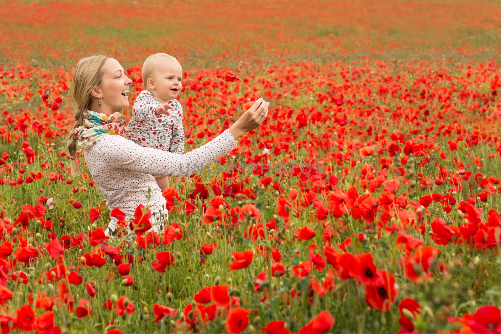Young mother and her daugher having fun in a meadow full of poppy flowers during a sunny afternoon