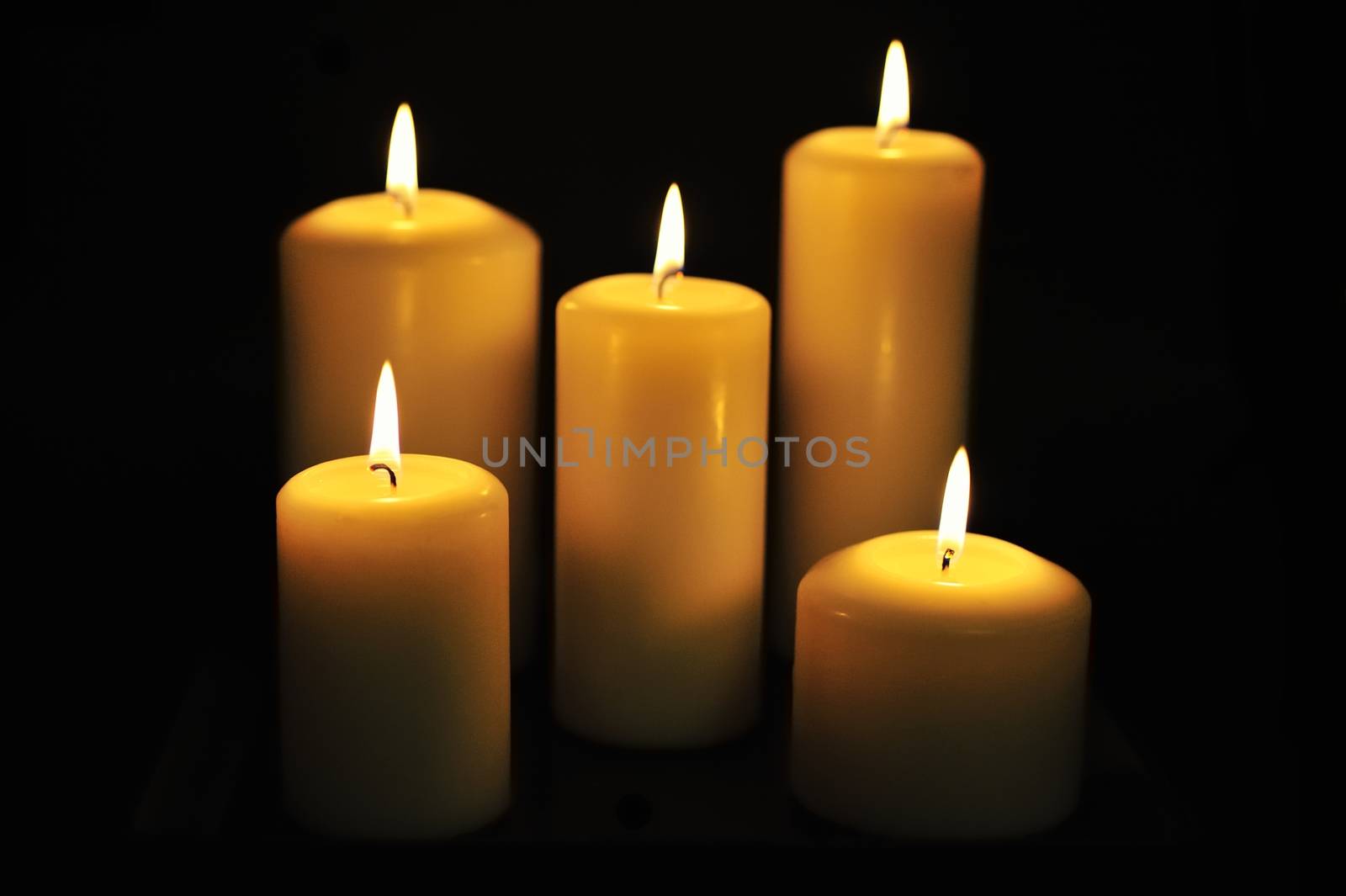 Five white candles on black background.