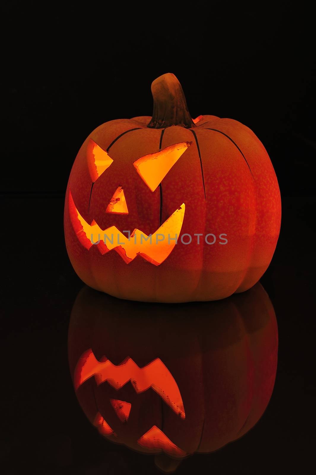 A candle lit and carved pumpkin casting a relection on a wooden floor.
