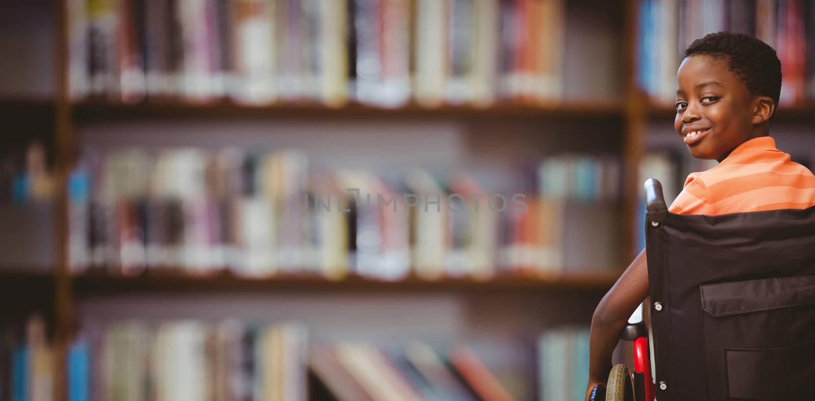 Portrait of cute boy sitting in wheelchair against library shelf