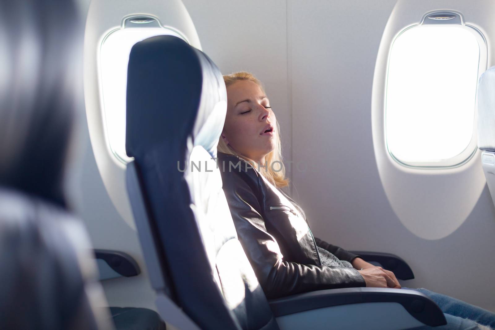 Tired blonde casual caucasian lady napping on uncomfortable seat while traveling by airplane. Commercial transportation by planes.