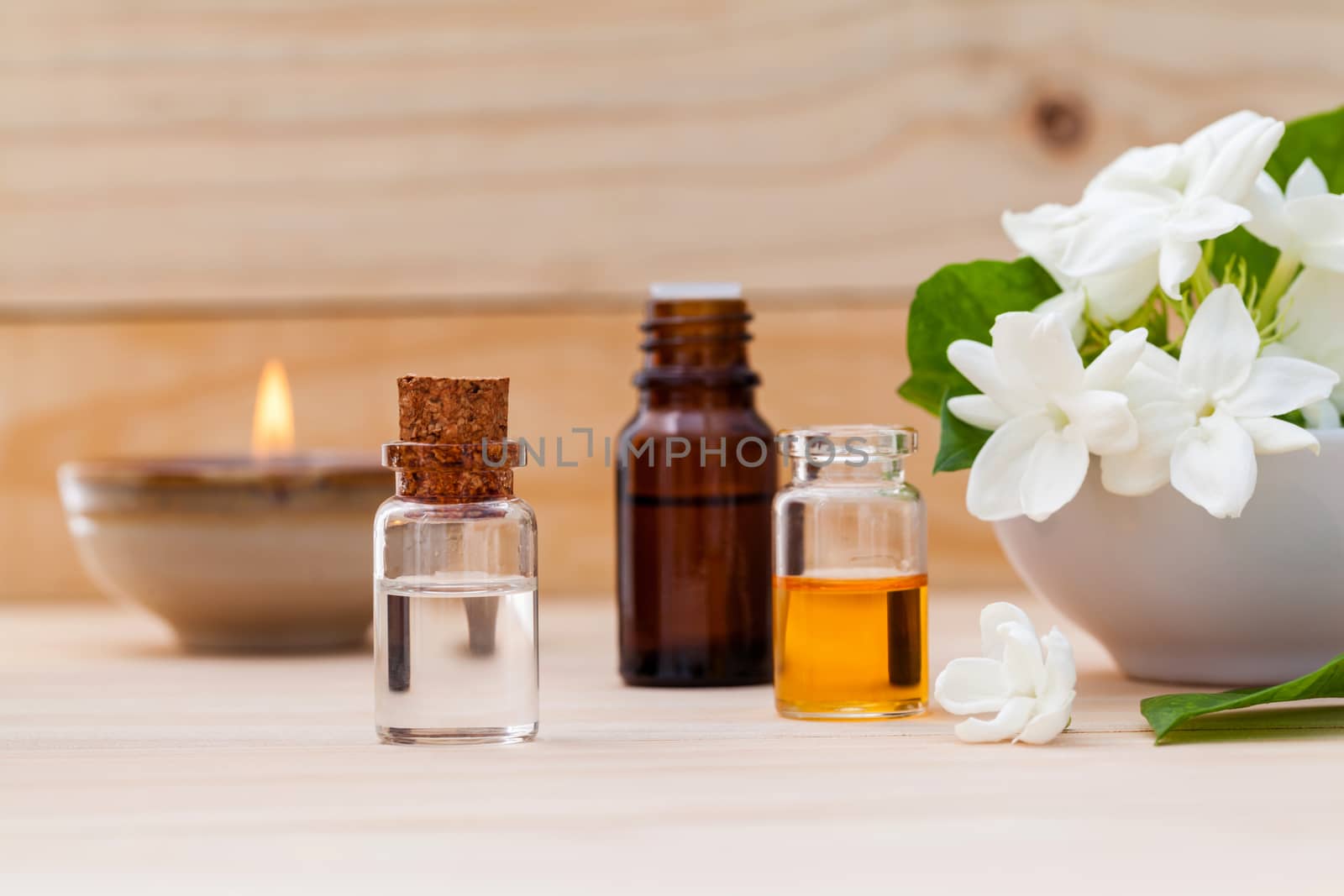 Aroma oil bottles arranged with jasmine flowers on wooden background .