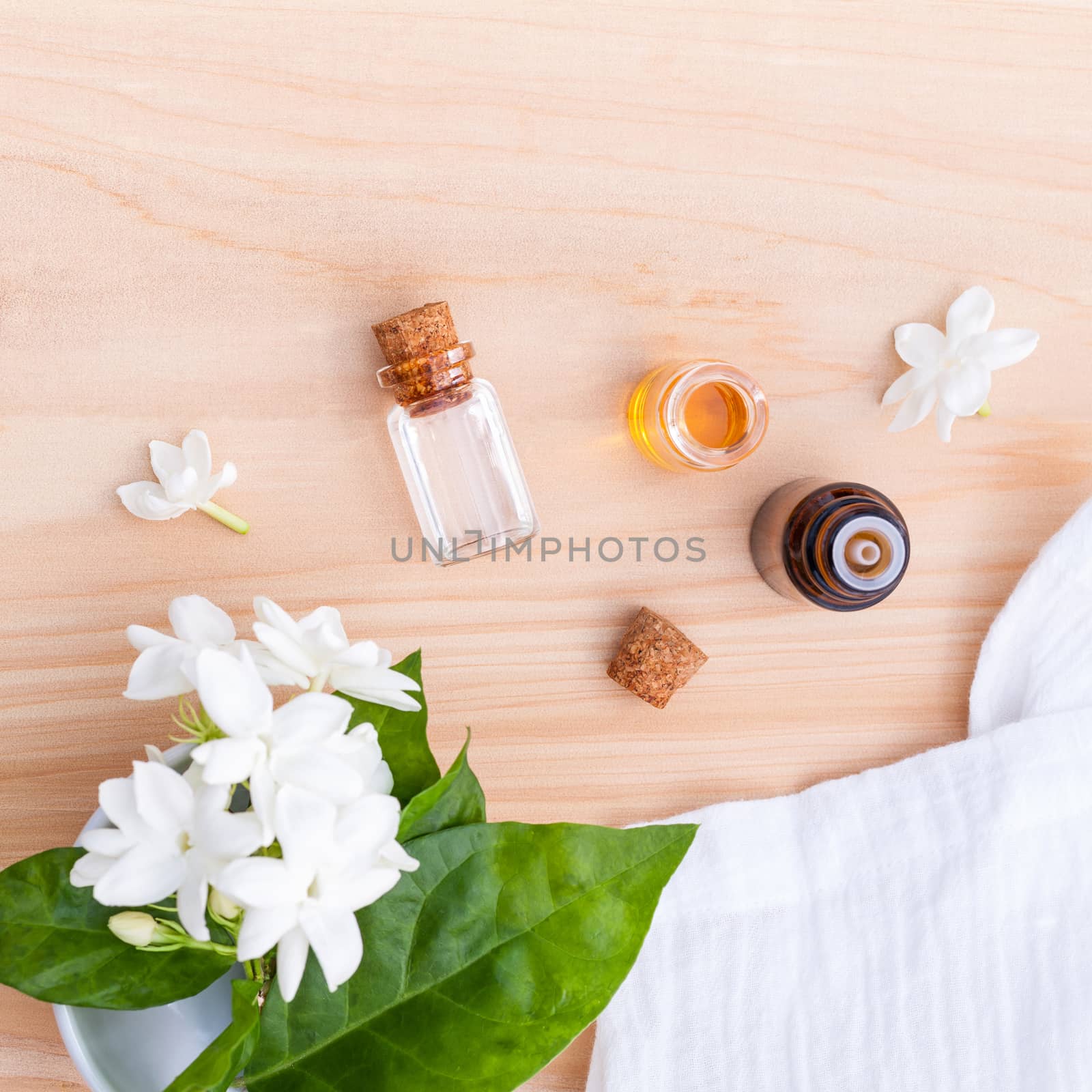 Aroma oil bottles arranged with jasmine flowers on wooden background .