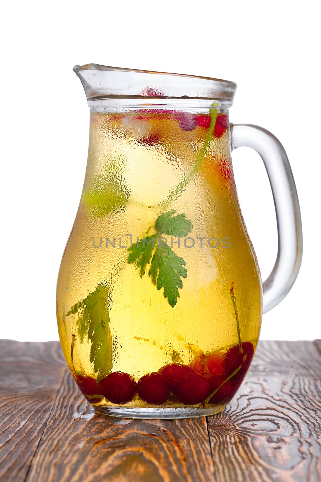 Glass pitcher of homemade spritzer (schorle) enriched with cherries and apple slices. Jug full of non-alcoholic sparkling and cold carbonated juice.