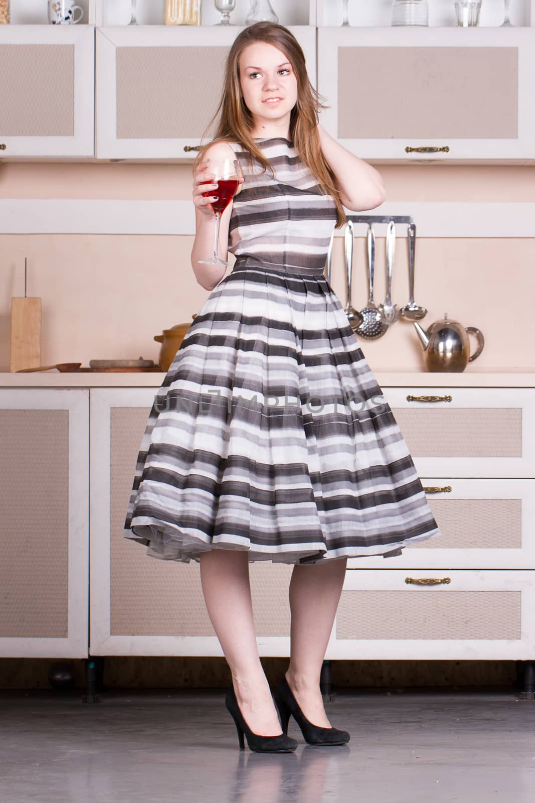 Attractive young woman in a dress holding a glass of wine in her kitchen.