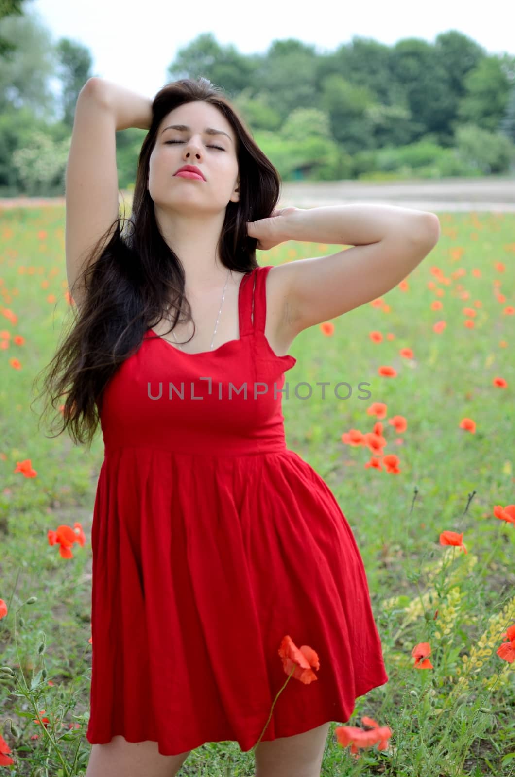 Female model standing in meadow, surrounded by poppies. Young girl with closed eyes, relaxing.