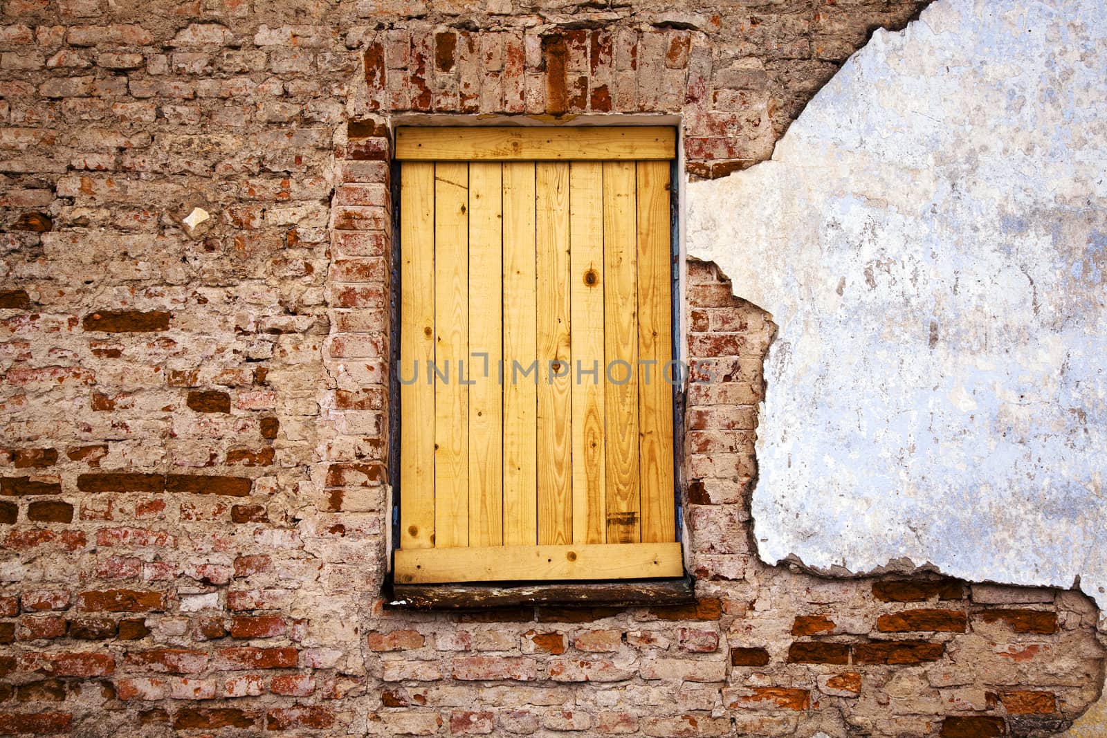   part of a wall of the ancient building. the window located in a wall is filled with boards